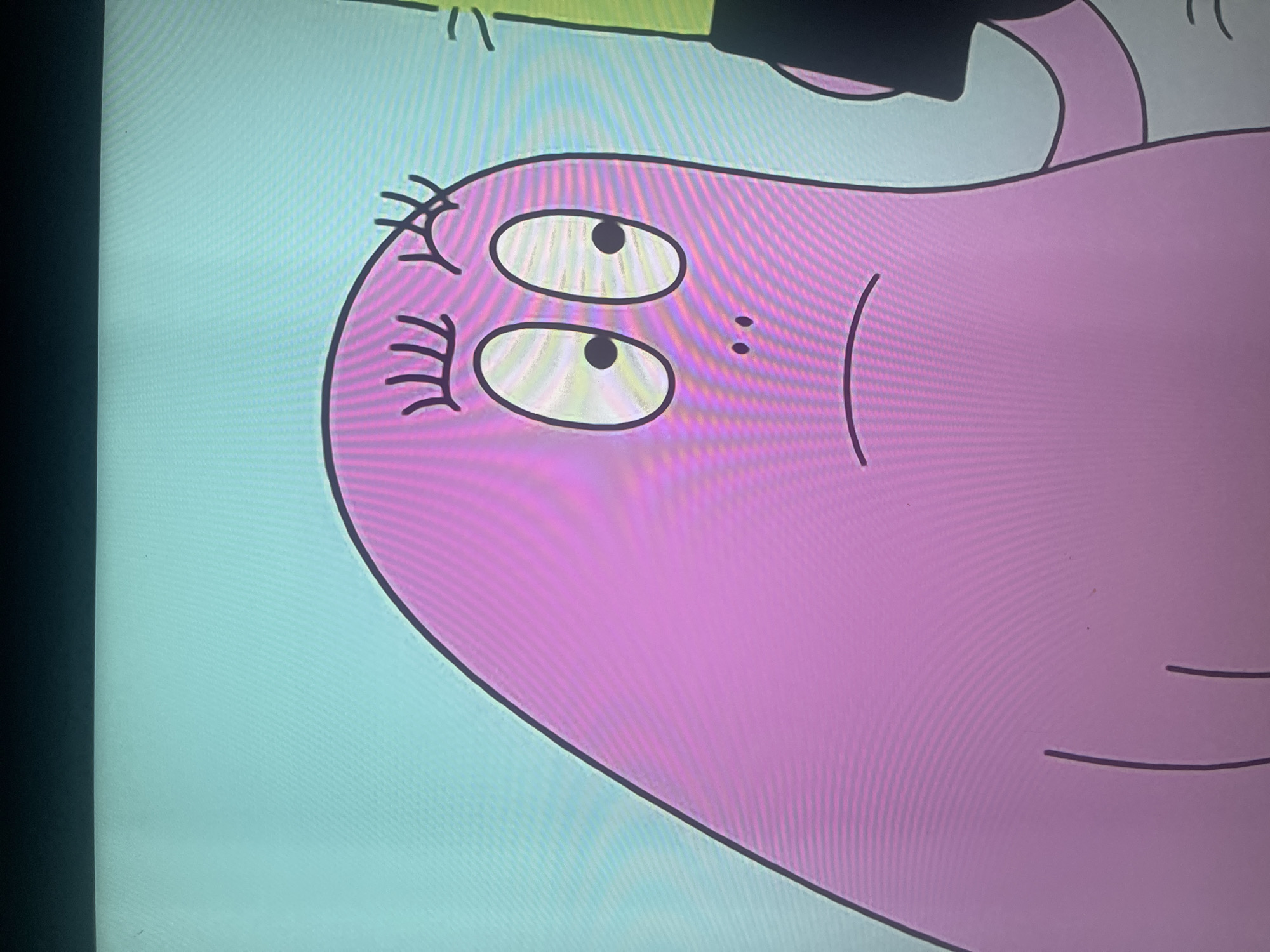 The image shows a close-up of a pink, cartoon character with large oval eyes and a small nose. The character has black eyelashes and a curved line for a mouth, suggesting a sad or worried expression. The background is a light blue, and part of a green object, possibly a stick or a toy, is visible on the right side of the frame, held by the character. The character appears to be on a flat, light-colored surface. There is no indication of the city of Ruse, Bulgaria, or any other geographical location within the image.