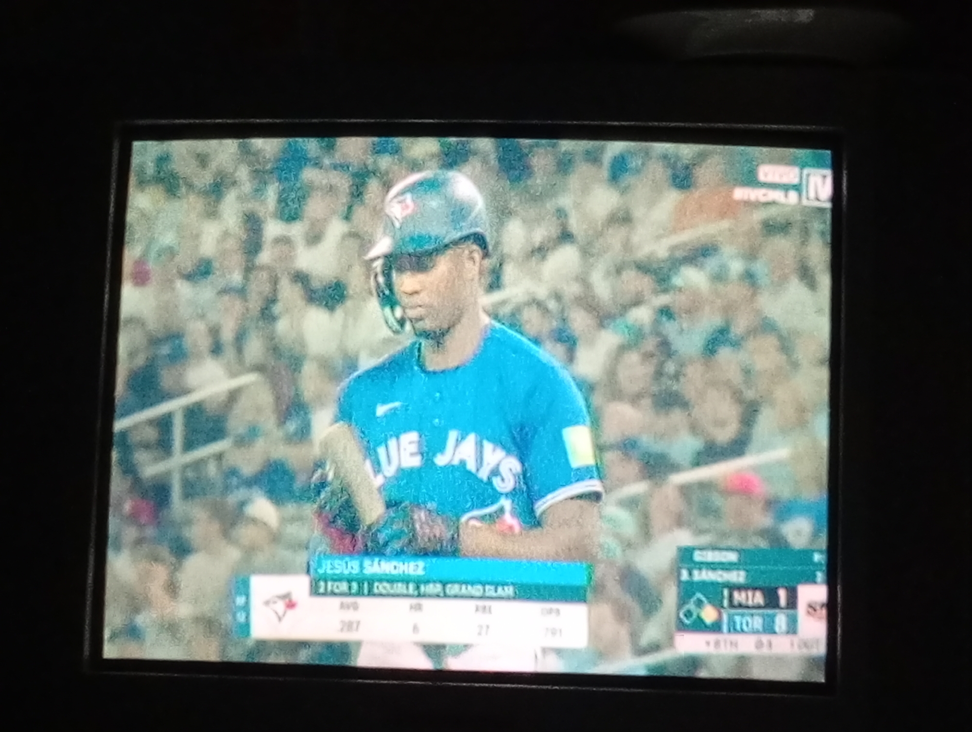 The image shows a television screen displaying a baseball game. The focus is on a Toronto Blue Jays player, Jesús Sánchez, at bat. Information displayed on the screen indicates his stats: a .287 batting average, 6 home runs, 27 RBIs, and a .791 OPS. The scoreboard shows Miami Marlins (MIA) at 1 and Toronto Blue Jays (TOR) at 8. The game is on Sportsnet. There is no indication of the location being Juan Griego, Venezuela.