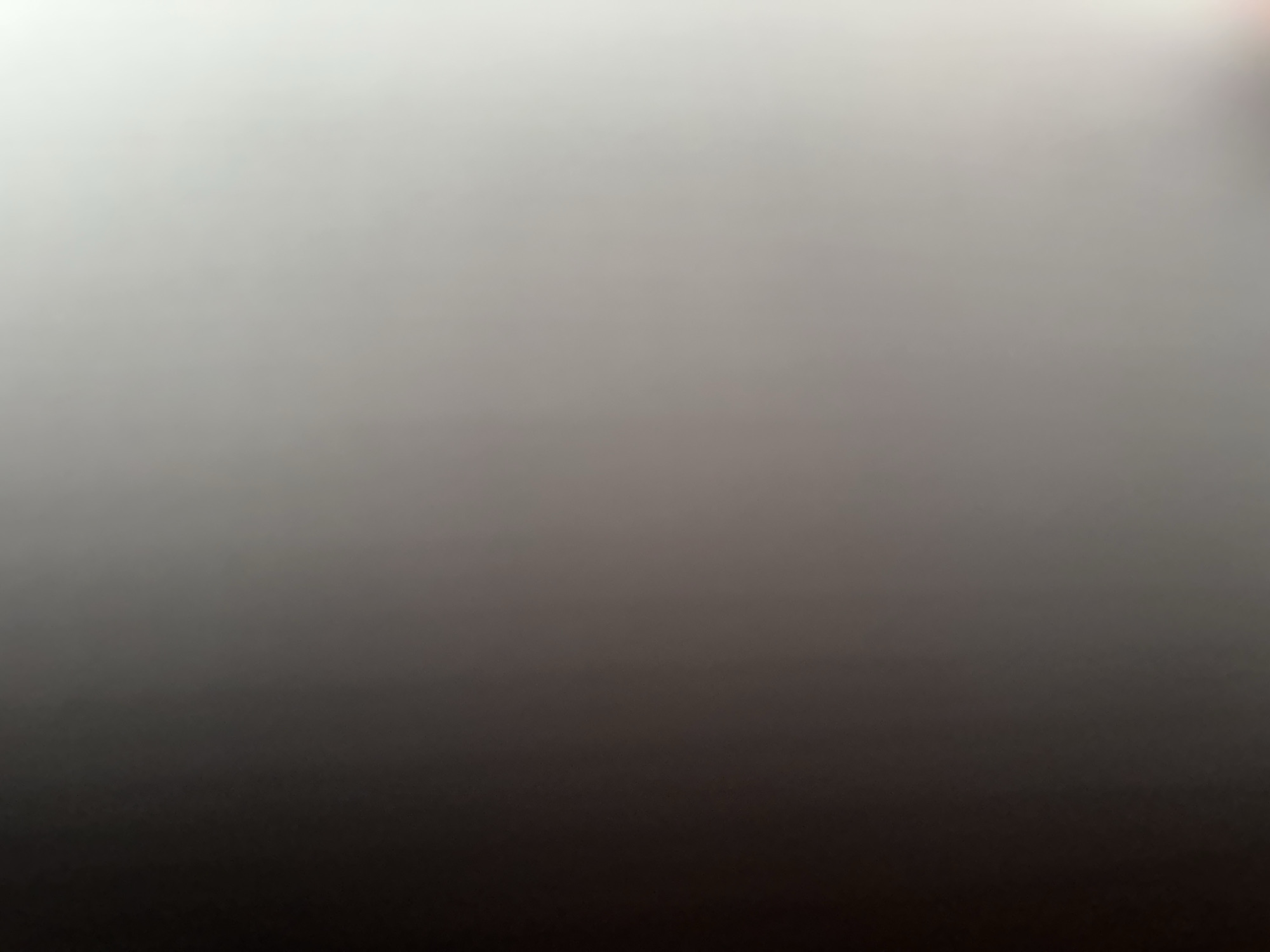 This is a blurry, abstract image with a gradient of light and dark tones. The top of the image is very light, appearing almost white, and it gradually transitions to a dark gray or black at the bottom. There are no discernible subjects, objects, scenes, or activities visible. The image is uniformly out of focus, making it impossible to identify any specific details. There is no indication of time of day, weather, location, or emotions. No text is visible in the image.