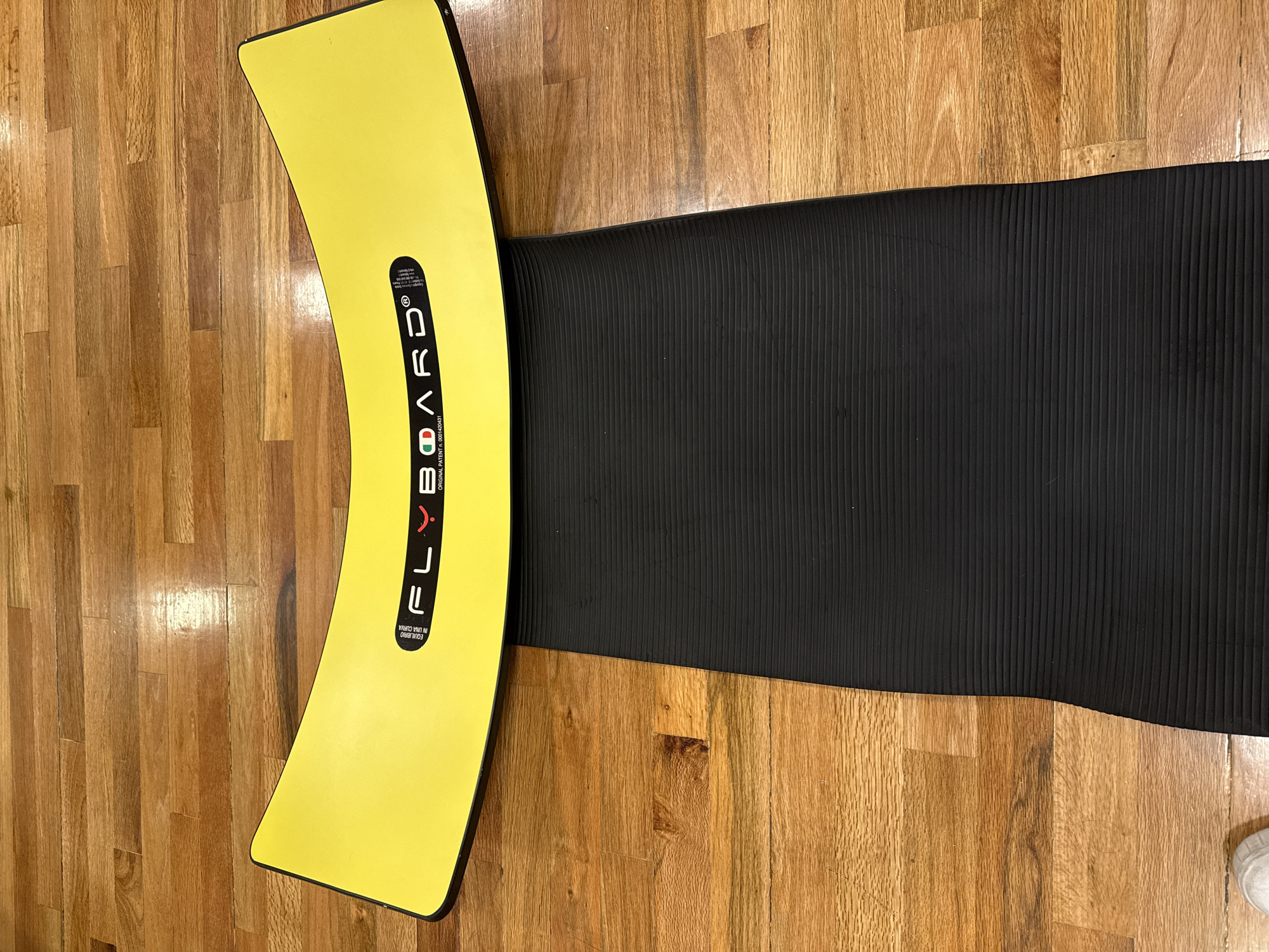 A yellow, curved, and branded FLEXBOARD lies on a black exercise mat, which is placed on a wooden floor. The location and city in Mexico are not evident from the image.