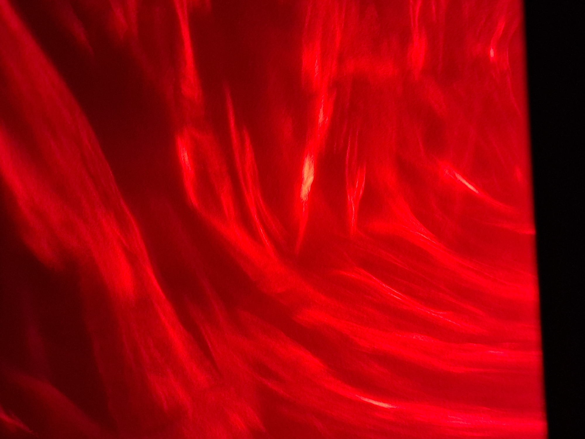 The image shows an abstract pattern of bright red light, resembling flowing or swirling liquid. There is a small area of yellowish light near the center. The right edge of the image is black, possibly indicating a border or the edge of a surface. The image does not contain information to identify the location in Novi Sad, Serbia, or any specific details about people, objects, actions, interactions, or environment.