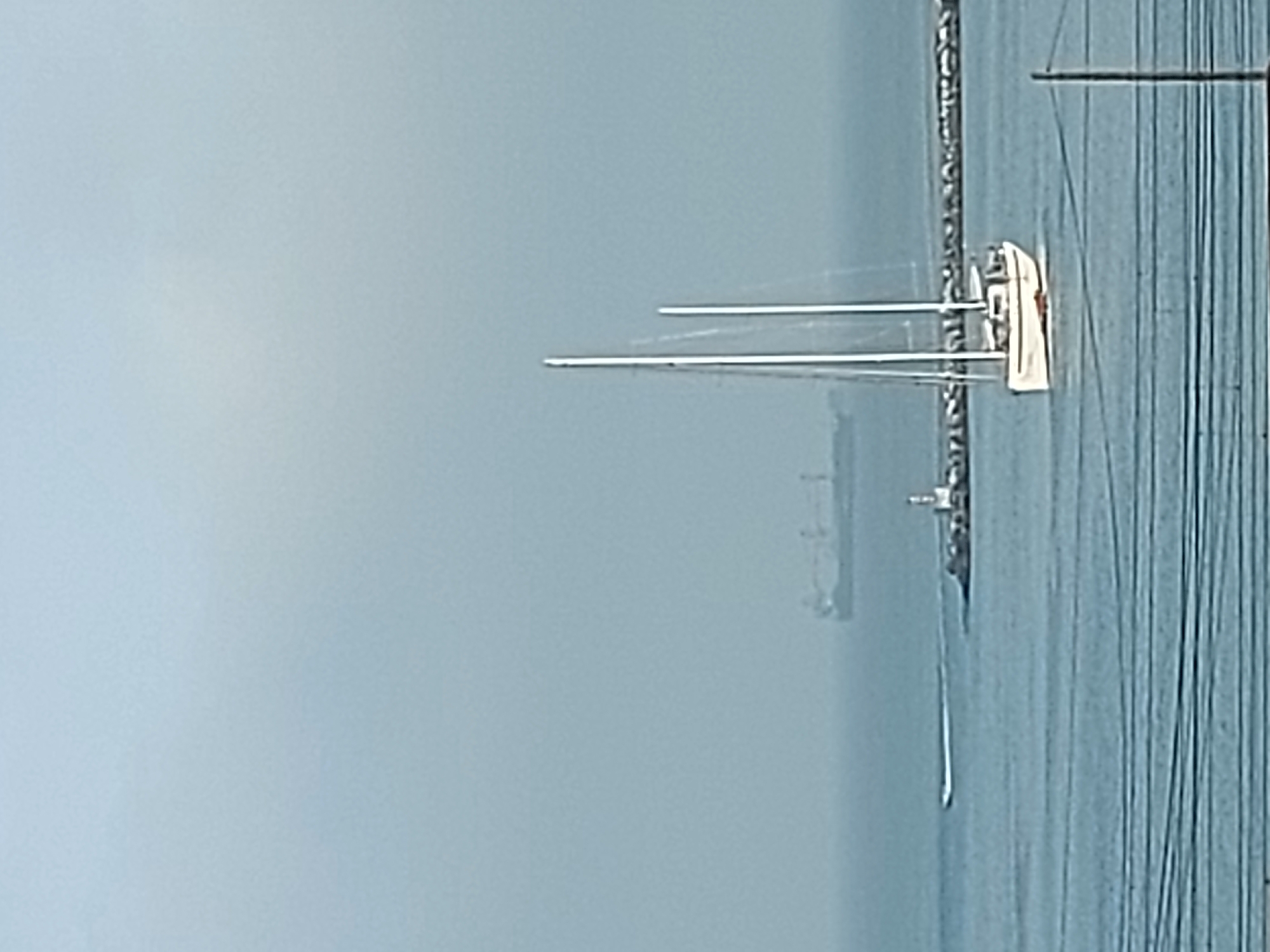 The image depicts a hazy scene on the water in Cascais, Portugal. A white sailboat with two tall masts is docked. In the background, there is a large container ship obscured by the mist, and a lighthouse near what appears to be a breakwater. There are many ropes in the foreground. The sky is overcast, and the water is a pale blue.