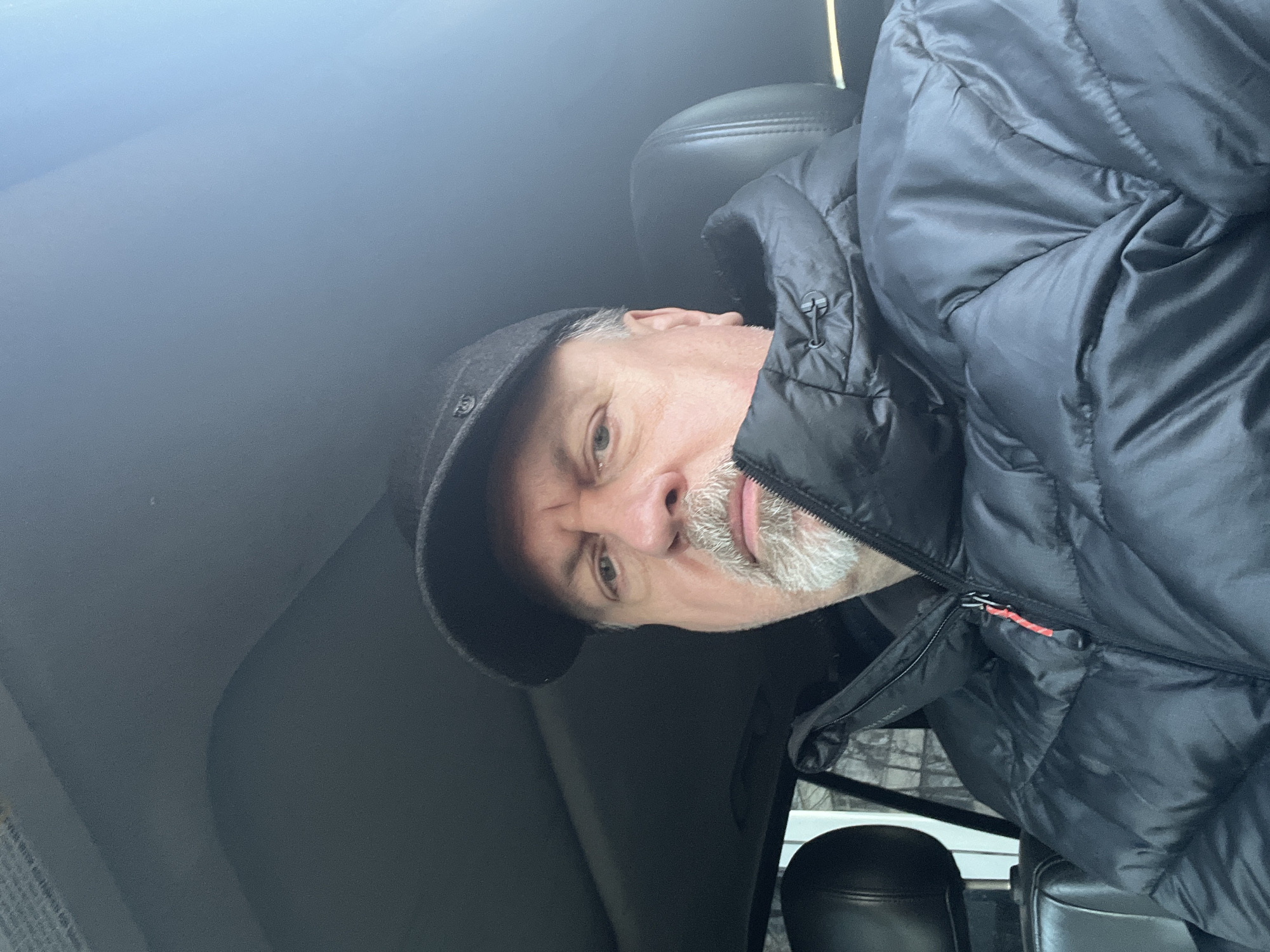 A selfie photograph of a middle-aged man wearing a dark-colored jacket and a dark cap. He appears to be sitting in a vehicle. The location is not identifiable as Podolsk, Russia based on the visual information provided in the image.