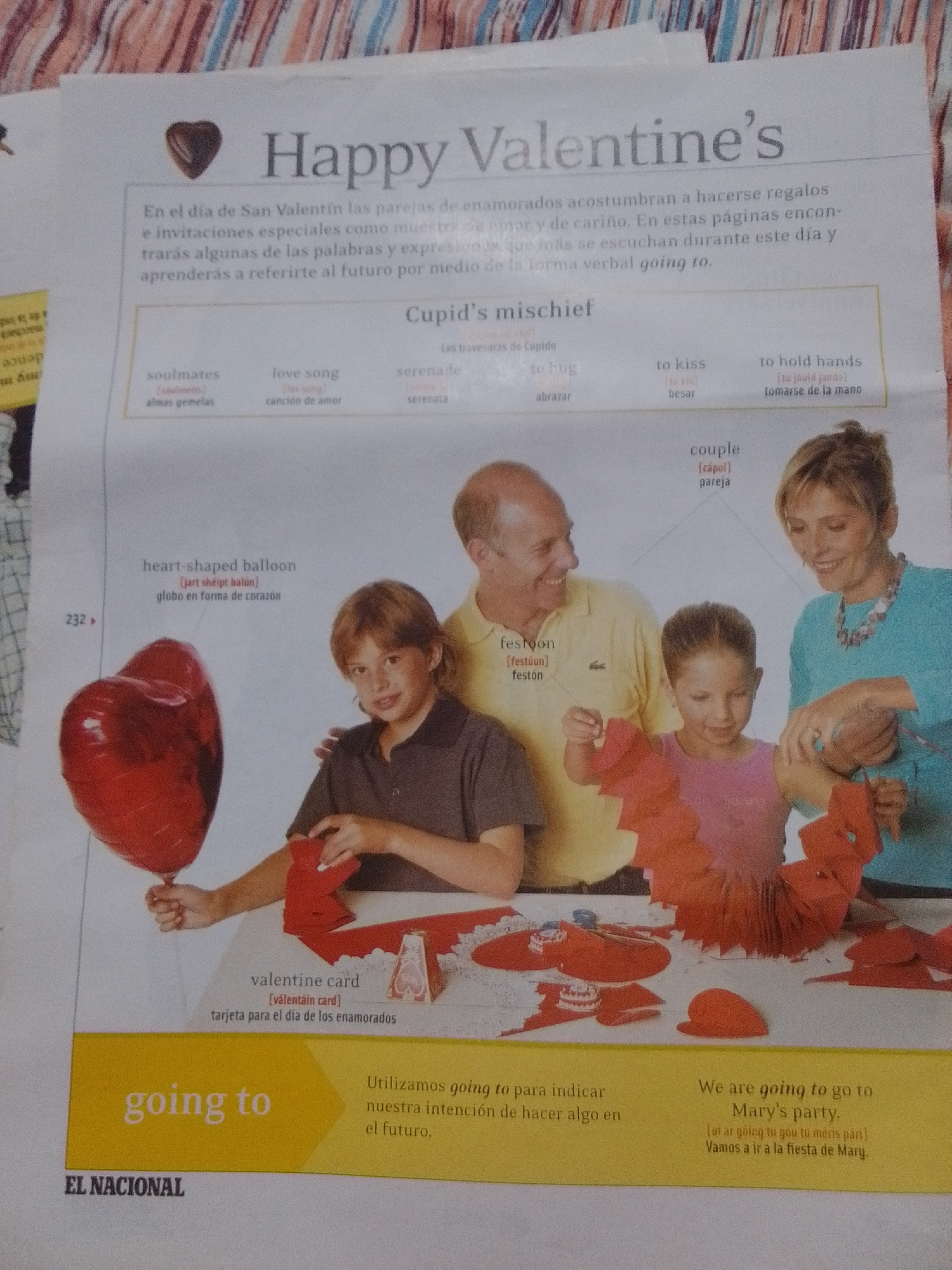 The image is a photograph of a newspaper page, likely from "El Nacional" based on the visible masthead. The newspaper article is about Valentine's Day, with the headline "Happy Valentine's". The page features several sections:
* **Textual content:** The main article discusses Valentine's Day traditions, gifts, and expressions of affection. There's a section titled "Cupid's mischief" which appears to be a vocabulary list with English and Spanish translations for terms like "soulmates", "love song", "serenade", "to hug", "to kiss", and "to hold hands". Another section defines "heart-shaped balloon" and "valentine card". There is also a smaller section in Spanish discussing the use of "going to" to indicate future intentions, and an English example sentence, "We are going to go to Mary's party."
* **Visual content:**
* A red, heart-shaped balloon is prominently displayed on the left side.
* A group of people, likely a family, are shown in the center and right of the image. This includes a man in a yellow polo shirt, a woman in a blue top, and a young girl in a pink shirt, who appears to be crafting something red and paper-like. Another child, a boy, is visible on the left, holding the balloon string.
* Various craft supplies, mostly red paper cutouts and a small Valentine's card or box, are spread on a table in front of the people.
The image does not contain any information about the city of La Tagua, Venezuela, nor does it depict any elements that would suggest a specific urban or geographical location. The scene appears to be indoors, possibly in a home or classroom setting where crafts are being made. The overall impression is one of a festive and family-oriented Valentine's Day theme.