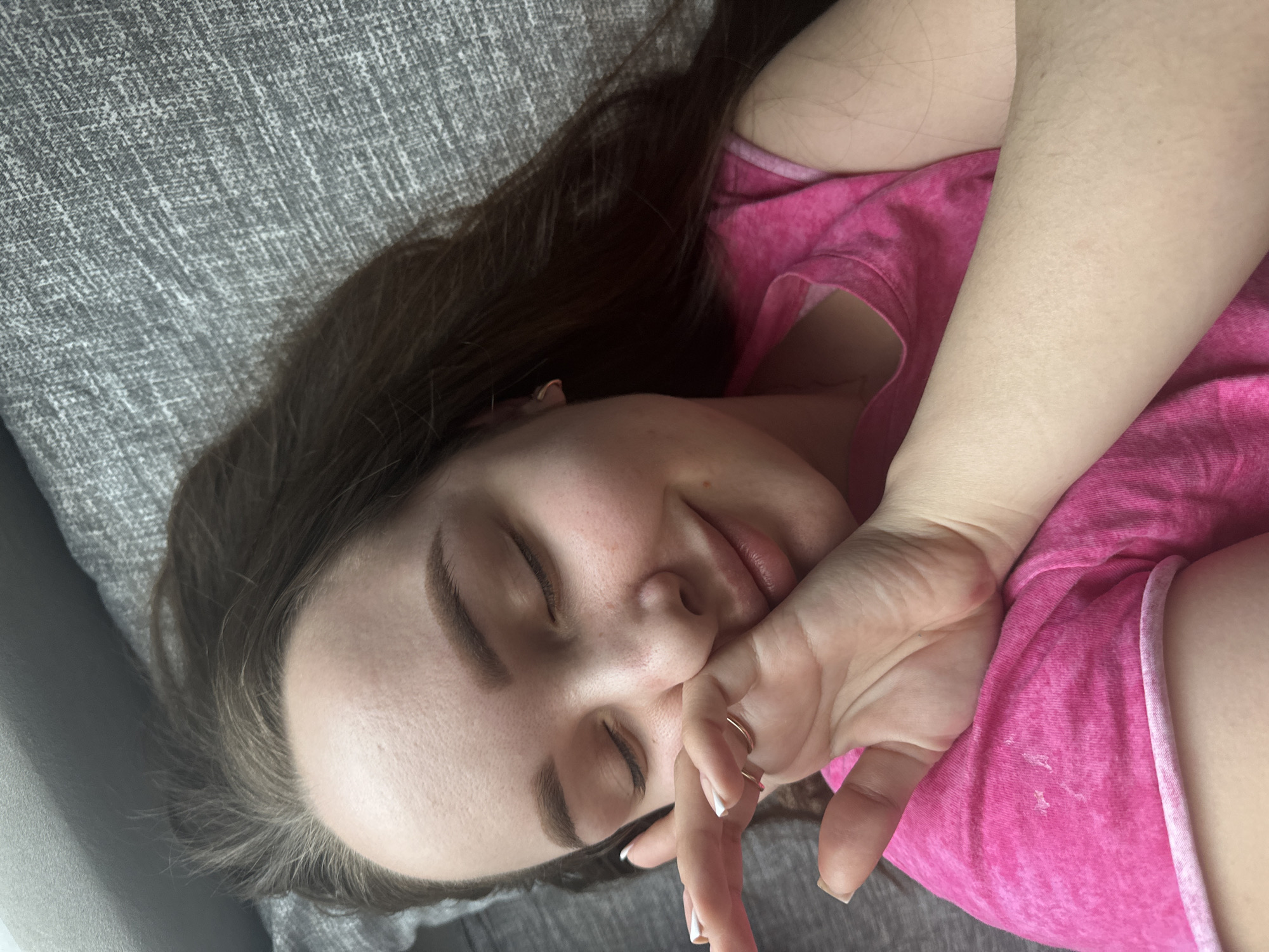 A woman with long dark brown hair, wearing a pink top, is lying on a gray textured surface. Her eyes are closed, and she has her hand near her face. The location cannot be determined as being in Chaikovsky, Russia.