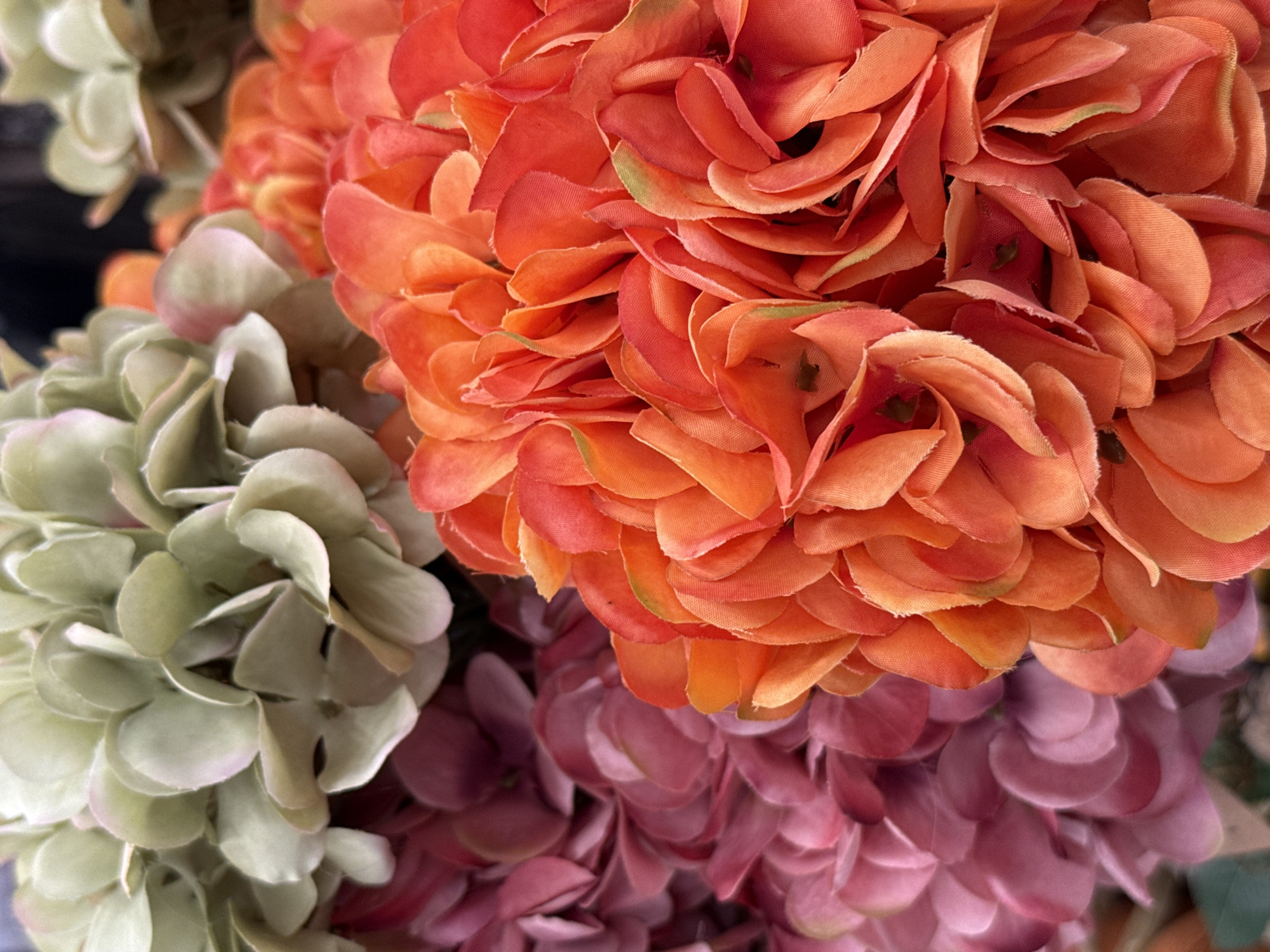 The image shows a close-up of artificial flowers in various shades of green, pink, and orange. The flowers are arranged in clusters, with some out of focus in the background and others in sharp focus in the foreground. The lighting is bright and even, suggesting an indoor setting. There are no people or animals visible in the image. The scene appears to be a retail display or a decorative arrangement. The location in Bad Lauterberg im Harz, Germany, is not discernible from the image itself.