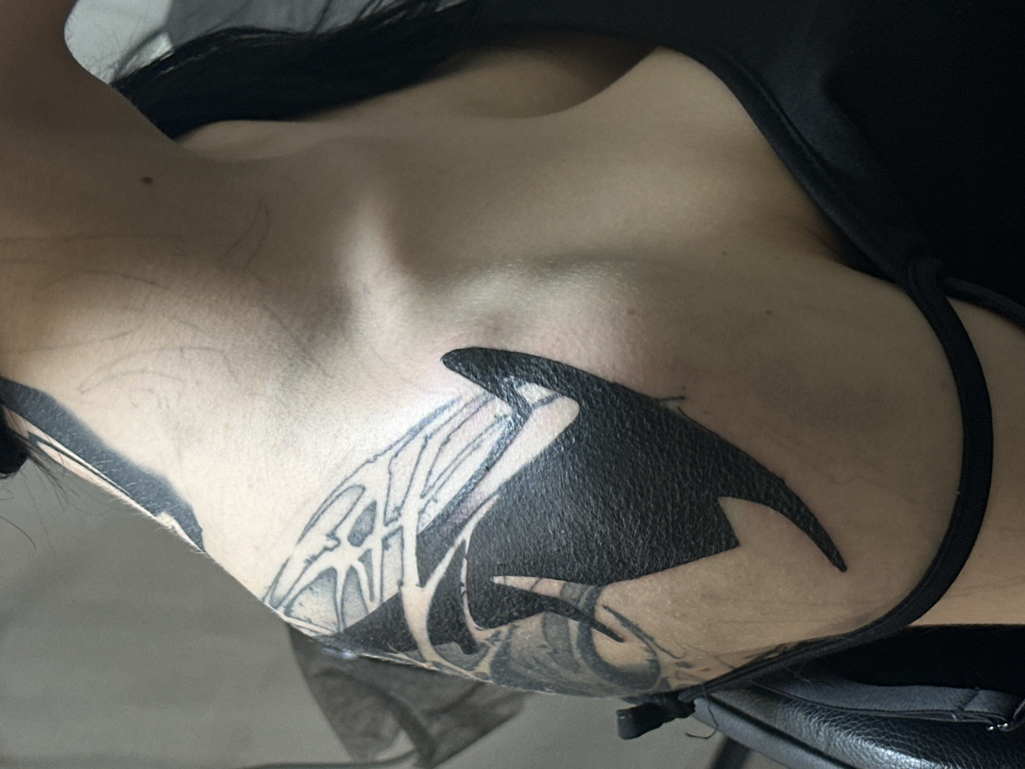 The image depicts a close-up view of a person's upper chest and arm. Visible on the person's skin is a large tattoo featuring a black and white orca design. The person is wearing a black garment with a thin strap that crosses over their shoulder. The background is out of focus and shows what appears to be dark clothing or possibly a dark surface like a chair. There is no discernible information about the location being Moscow, Russia.