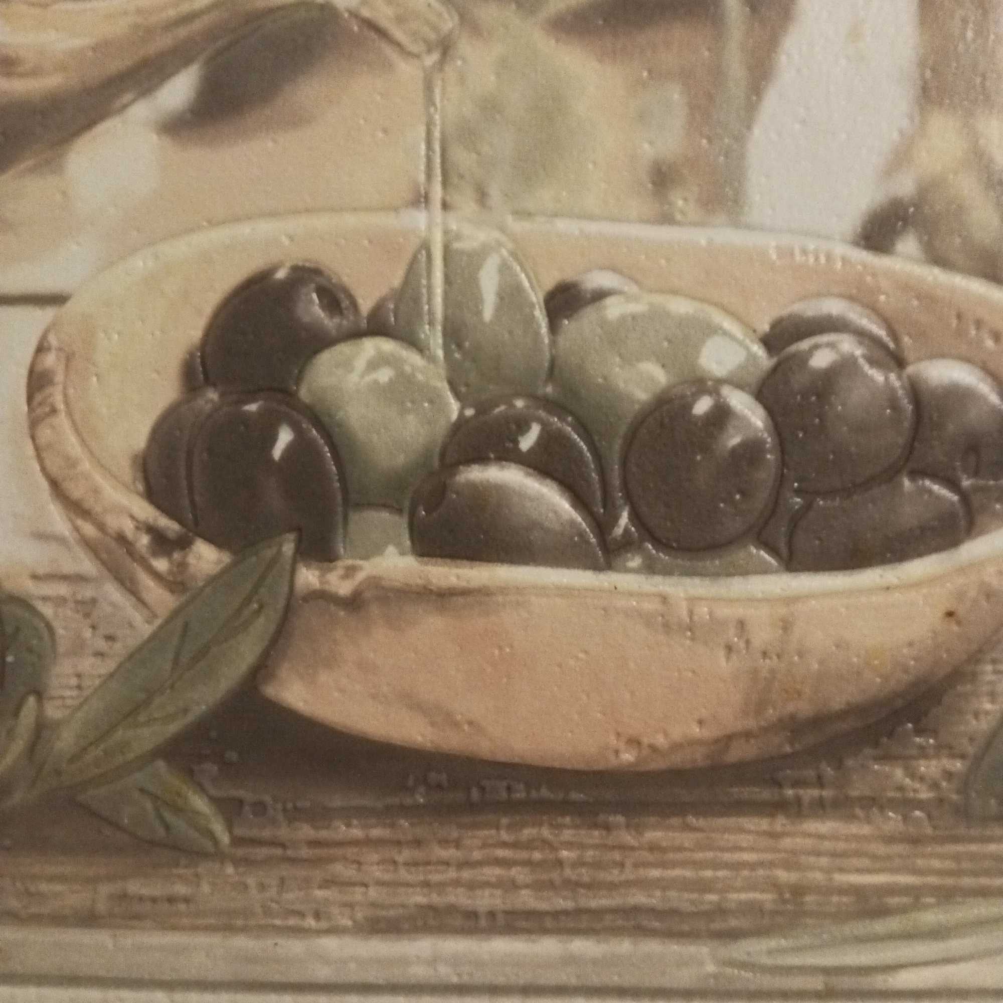 The image is a close-up shot of a ceramic tile depicting a bowl of olives. The bowl, rendered in a rustic brown color, is filled with a mix of green and black olives, some of which appear to be glistening, possibly from olive oil being poured over them. A stream of oil is visible as it descends into the bowl. The foreground also shows a few olive leaves. The tile is set against a background that appears to mimic a wooden surface. The overall color palette is dominated by earthy tones. The image does not provide any information that would link it to the city of Chaikovsky, Russia. There are no people in the image. The subjects are olives and olive oil, and the primary object is a ceramic bowl. The main action captured is the pouring of olive oil. The environment is depicted as a rustic setting, potentially suggestive of Mediterranean themes or cuisine.