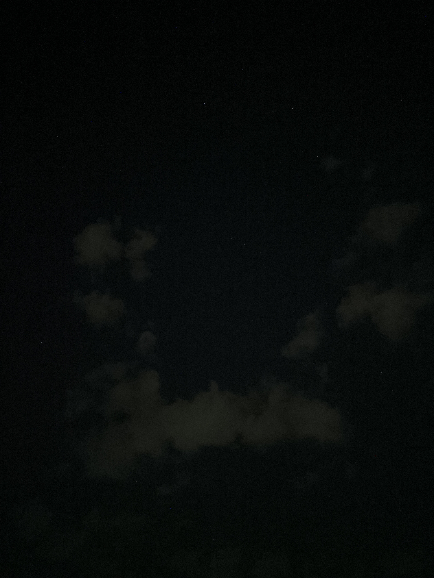 This is a nighttime photograph of the sky, showing scattered clouds and a few visible stars against a dark, black background. The clouds are illuminated from below by an unseen light source, giving them a faint, grayish-white appearance. The overall scene is dark and somewhat featureless, with no discernible objects or structures on the ground. The image was captured in Chișinău, Moldova.