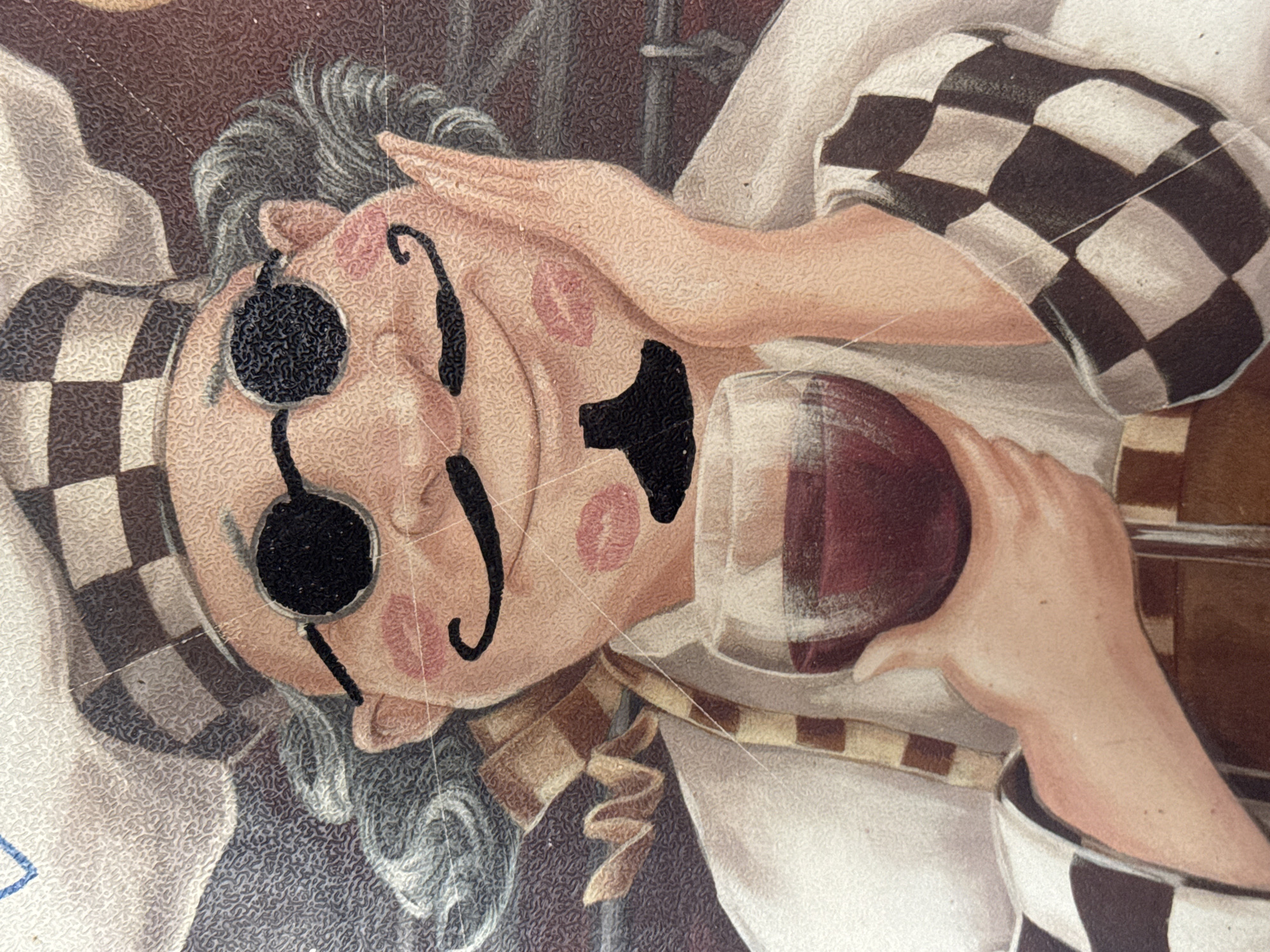 The image is a close-up of a cartoonish drawing of a chef. The chef is wearing a checkered hat and apron, round sunglasses, and has a curled mustache and a small goatee. There are pink kiss marks on the chef's cheeks and chin. The chef is holding a glass of red wine in their left hand. The background is textured and appears to be a reddish-brown color. The location in the city of Zaokskiy, Russia is not discernible from the image.