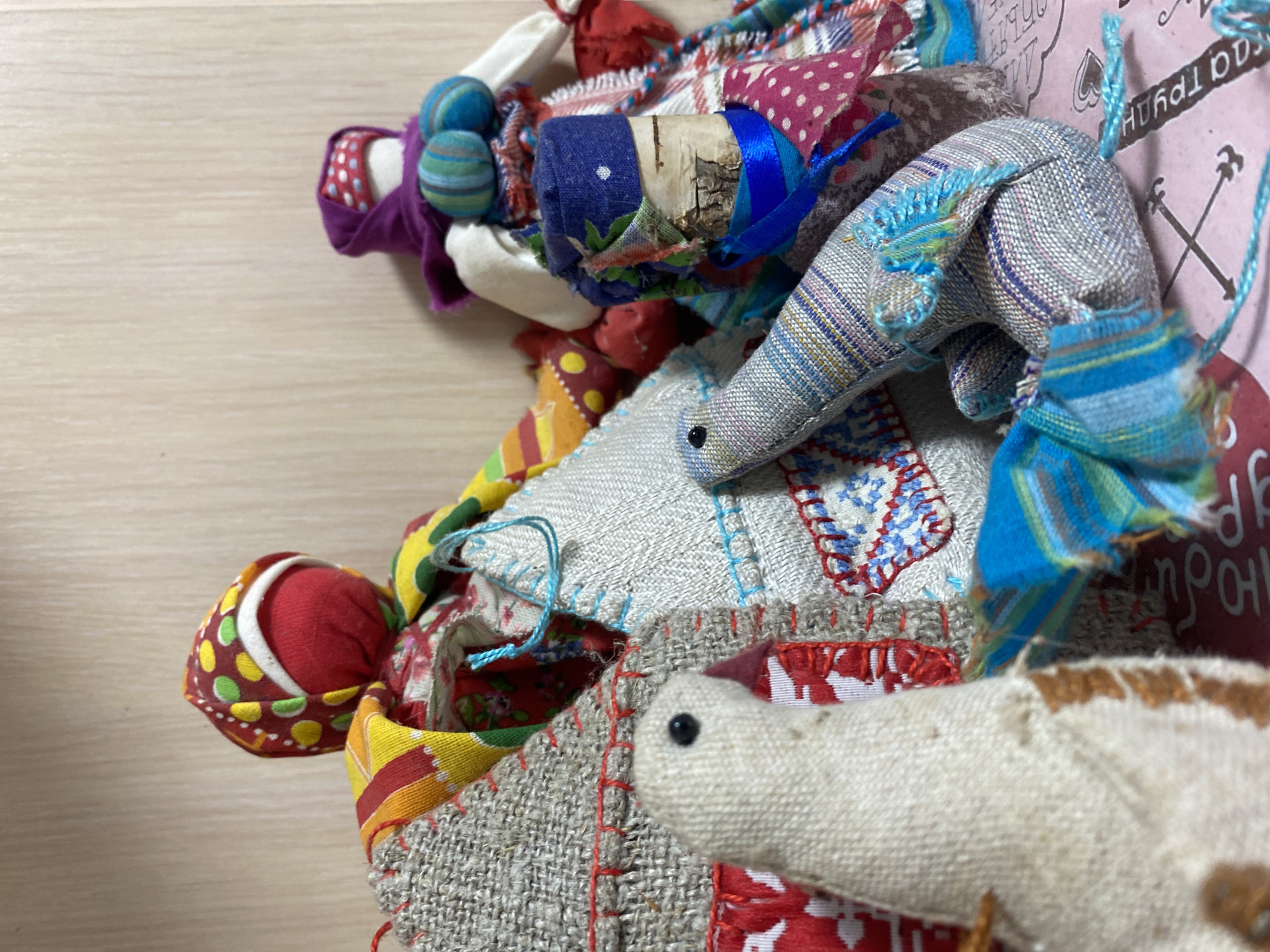 The image shows a collection of handmade rag dolls and fabric pieces. There are dolls of various shapes and sizes, constructed from colorful, patterned fabrics and adorned with details like beads, ribbons, and embroidery. The patchwork suggests that the items may be folk art or children's toys. The text in the background indicates a location in Ольховка, Russia.