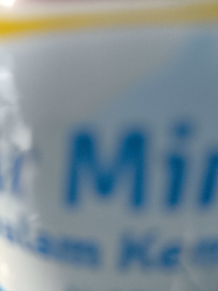A close-up, blurry image of the word "Min" in blue letters on a white surface. The image is out of focus, making it difficult to discern any other details. The location of the image cannot be determined from the image itself.