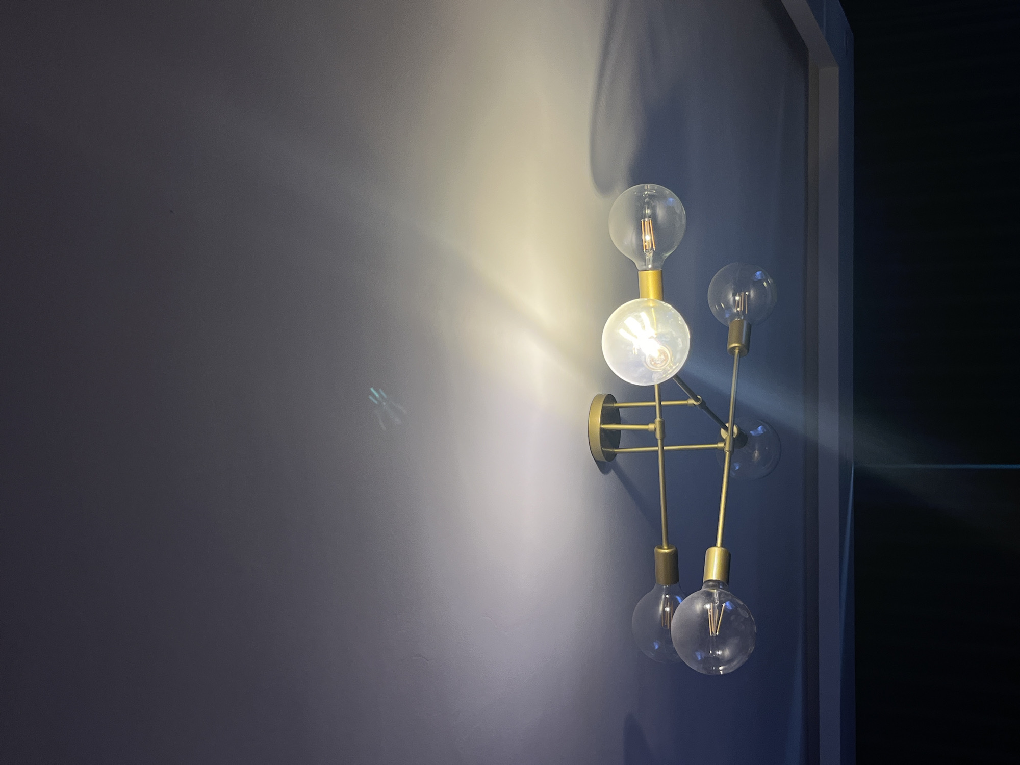 The image shows a modern chandelier with multiple Edison-style bulbs attached to brass arms. The chandelier is mounted on a dark blue ceiling, and the light from the bulbs casts shadows and reflections on the ceiling. There are no people or any other objects visible in the image. The location in the city of Varna, Bulgaria, is not discernible from the image.