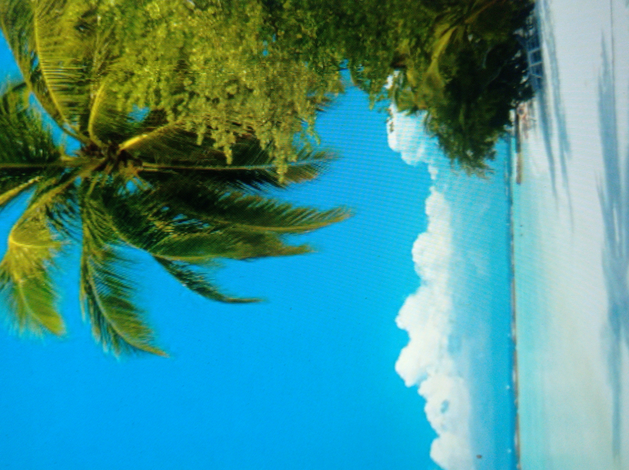 The image depicts a tropical beach scene with a bright blue sky, palm trees, white sand, and turquoise water. Clouds are visible in the distance. The scene appears serene and tranquil. There are no people visible in the image. The location of this image is not in the city of Mukachevo, Ukraine, as Mukachevo is an inland city and does not have beaches or palm trees.
