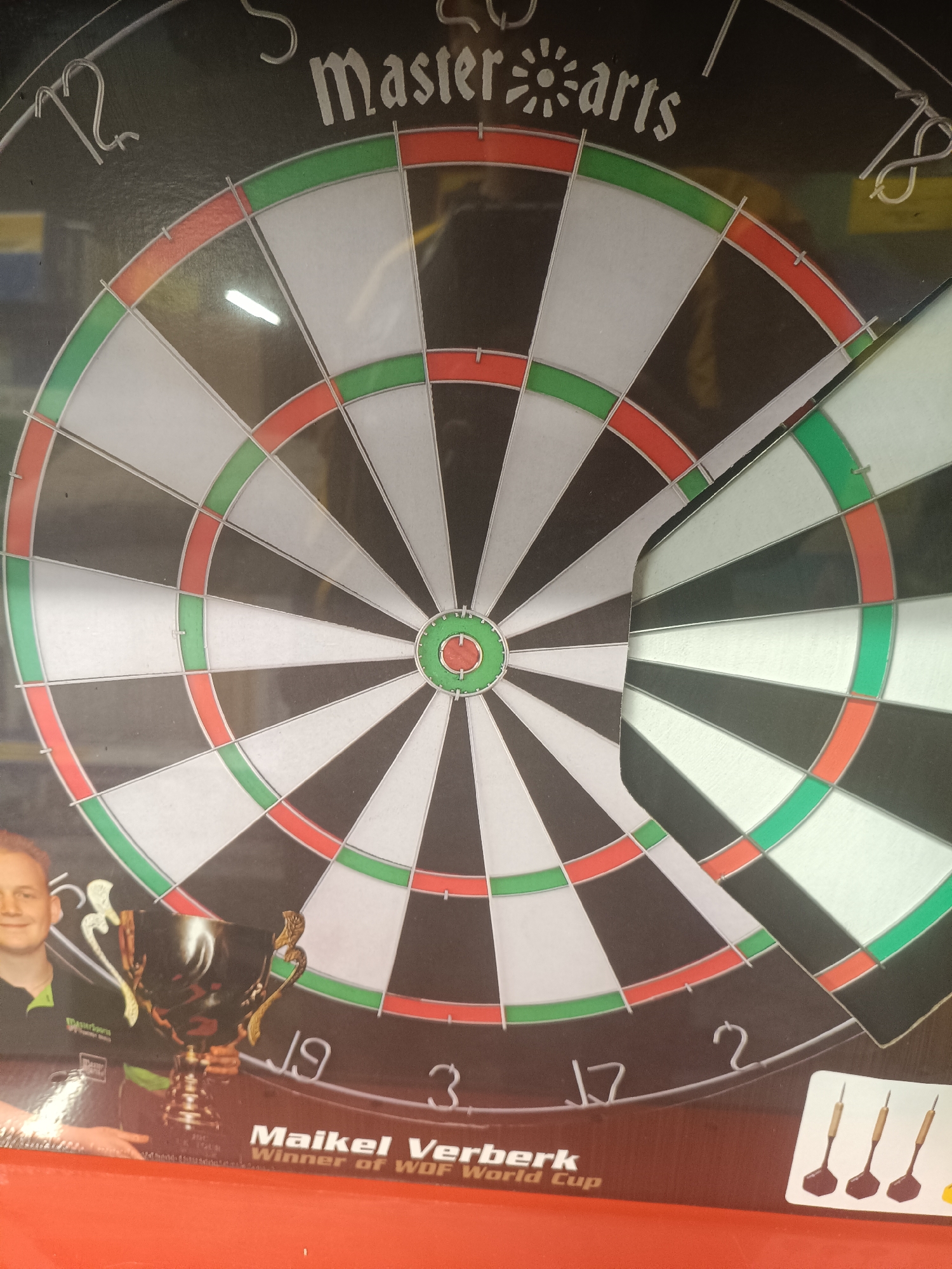 The image shows a dartboard with the words "Master darts" at the top. Below the dartboard, a man named Maikel Verberk is pictured holding a trophy. Text below his image reads "Winner of WDF World Cup." The dartboard has numbers from 1 to 20 around its circumference, with red and green sections. There are also three darts depicted in the bottom right corner. The overall scene suggests a sporting event or advertisement related to darts. The location in Narva, Estonia is not evident from the image.