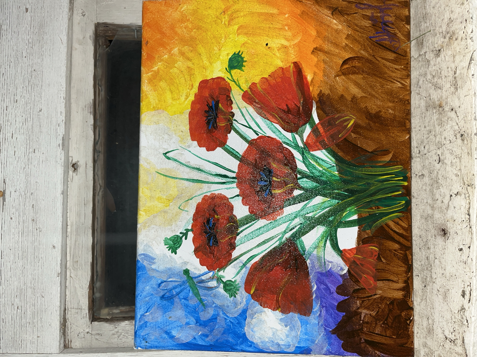 An acrylic or oil painting on canvas, featuring a vibrant bouquet of red poppies with green stems, is depicted leaning against or placed next to an old, weathered white wooden window frame. The painting occupies the right side of the image, while the window frame and a dark window opening are on the left.
The painting's background transitions from a bright yellow and orange at the top, fading into white in the middle, and then into shades of blue and purple at the bottom left. The top right portion of the background is a rich brown. The poppies are rendered in various stages of bloom, with some showing dark blue or black centers and others appearing as closed buds. Visible brushstrokes give the painting a textured quality. A small green insect, possibly a dragonfly, is painted near a poppy bud in the bottom left corner. An illegible signature, appearing in purple script, is visible in the top right corner of the painting against the brown background.
The window frame is made of aged wood with chipped white paint, revealing some of the darker wood beneath. It shows signs of wear and tear, including cracks and dirt. Behind the frame, a dark, rectangular opening suggests a window pane or a void, with faint reflections indicating it might be glass. The setting appears rustic or old, with the painting positioned vertically. No activity or event is taking place; it is a still depiction.