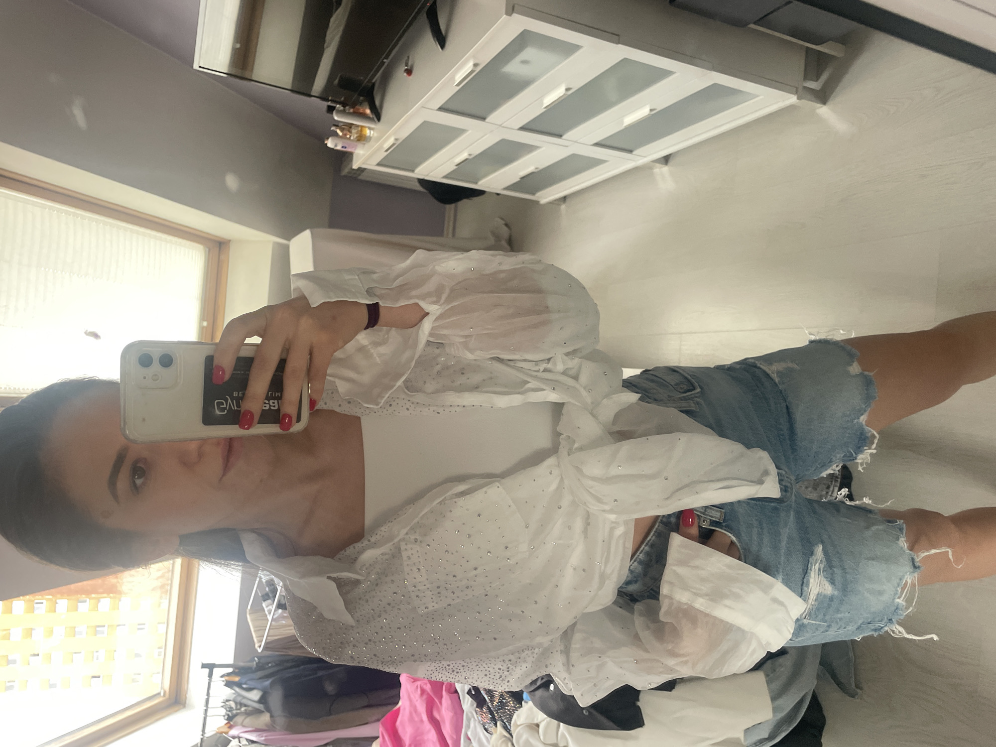 A woman is taking a selfie in what appears to be an indoor setting. The background features a room with a window on the left, a wardrobe and furniture. The location can't be determined as Sofia, Bulgaria.