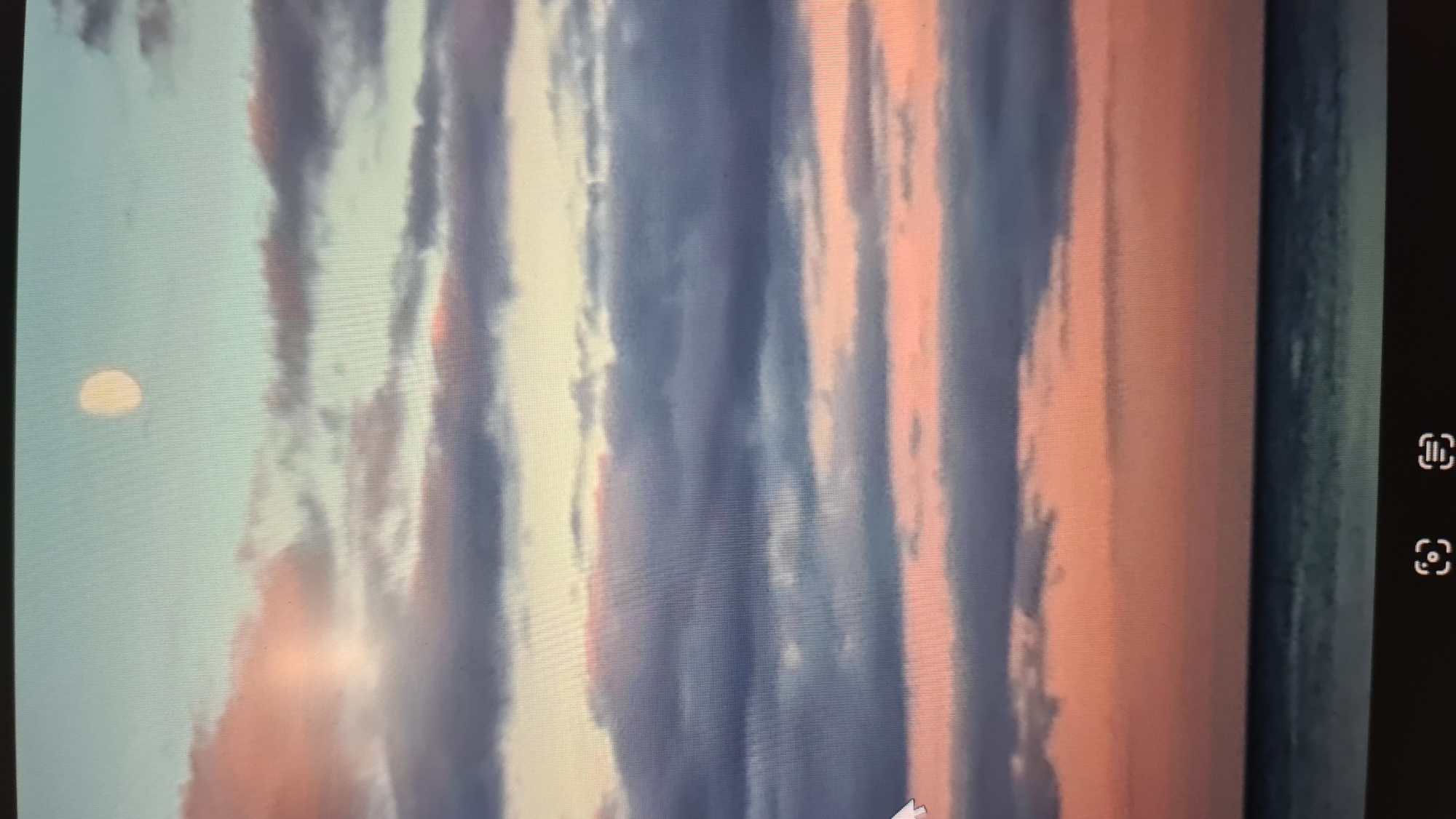 The image shows a serene sunset over the ocean. The sky is filled with layers of clouds, tinged with hues of pink, orange, and purple, gradually fading into a soft blue at the top. A pale, round moon is visible in the upper portion of the sky. Below the sky, a calm ocean stretches across the horizon, its surface reflecting the colors of the sunset. The overall atmosphere is tranquil and picturesque.