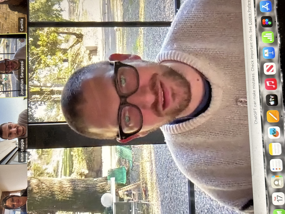 A screenshot captures a Zoom meeting with several participants, including Eitan Caggia, Jonathan Saragossi, and Camilla. The main focus is a man wearing glasses and a sweater, possibly the speaker. A laptop dock is visible, featuring icons for apps like Safari, Google Chrome, Apple TV, and more. A warning about ChatGPT potentially making mistakes is displayed at the top of the screen. The date "Tue 17" is also present.