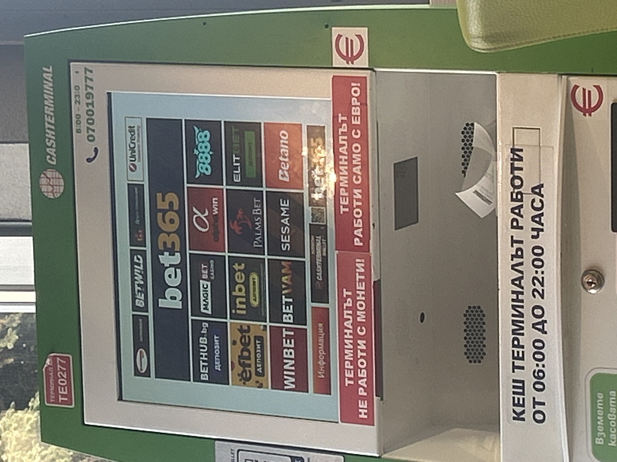This is a close-up, tilted image of a "CASHTERMINAL" in Varna, Bulgaria, identifiable by the Bulgarian text. The terminal's screen displays logos of various betting and gambling platforms like "bet365", "8888", "WINBET" and others. The terminal operates between 06:00 and 22:00 and accepts only Euros. A sign says that it does not accept coins. There are signs for euro currency, cash, and a telephone number.