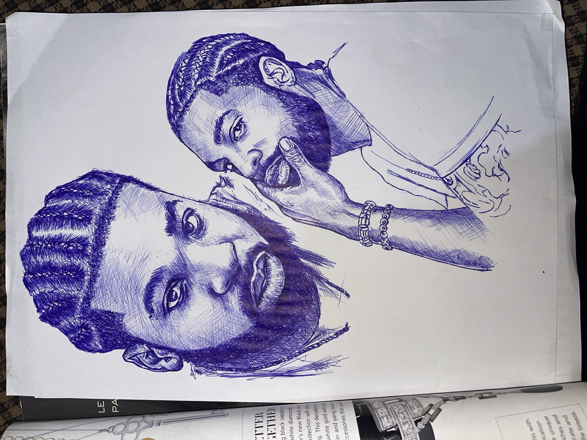 The image is a blue ink sketch on white paper, featuring two portraits of men. The man on the left is larger and closer to the viewer, with his head turned slightly forward. He has a full beard and cornrowed hair. The man on the right is smaller and appears to be in the foreground, with his head tilted and his hand touching his mouth. He also has a beard and cornrowed hair. Both men are depicted with intense gazes. The sketch includes details such as jewelry on the man on the right, specifically bracelets. The paper is placed on a dark, textured surface, possibly a rug or cloth. To the left of the sketch, a portion of a magazine page is visible, showing text and an image of diamond jewelry. There is no information within the image that indicates a specific location in Jos, Nigeria.