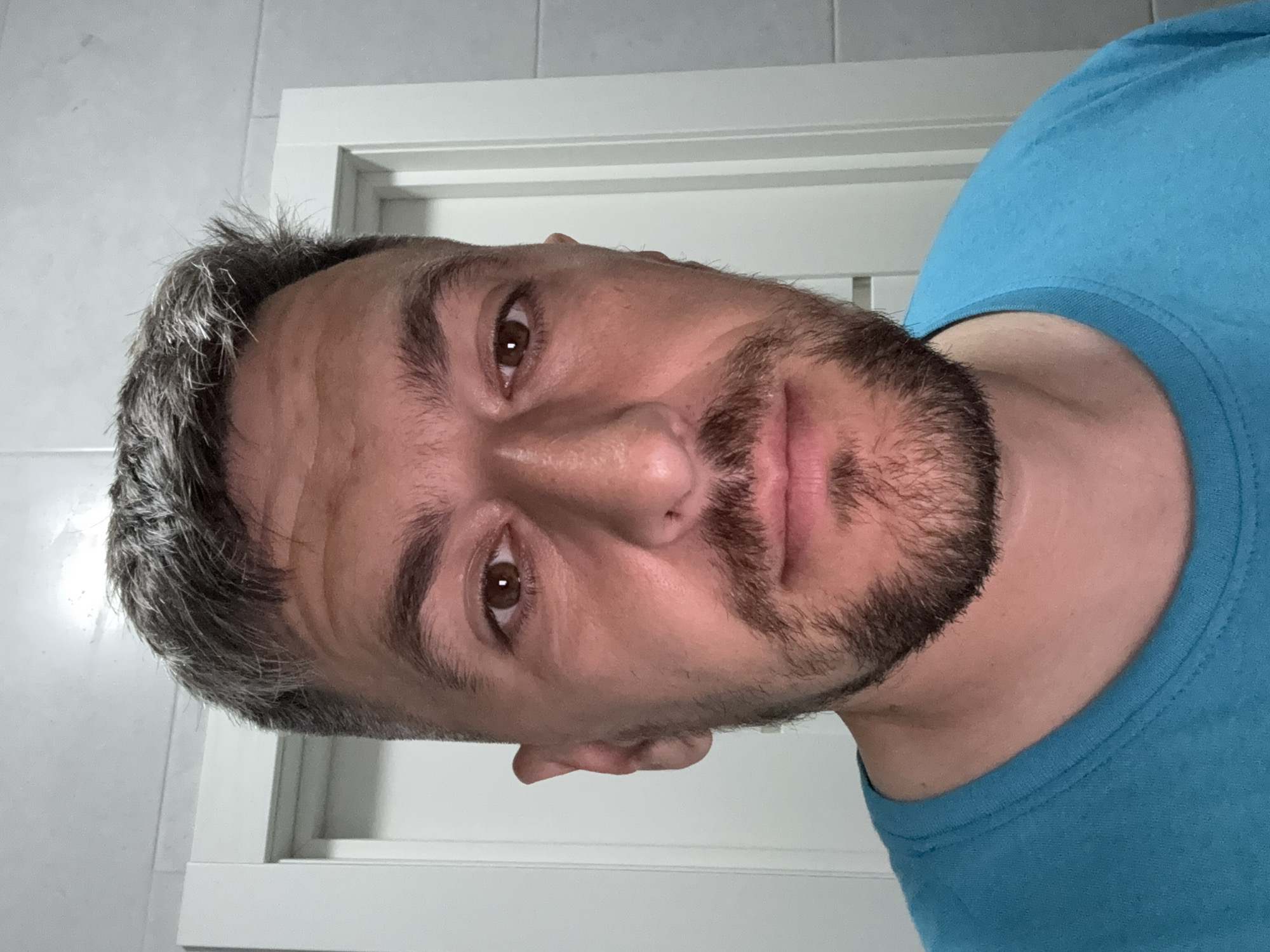 A head-and-shoulders portrait of a middle-aged man with graying hair and a beard, wearing a blue t-shirt. The background includes a white door with molding and a light-colored wall. No information indicates the location of Rostov-on-Don, Russia.