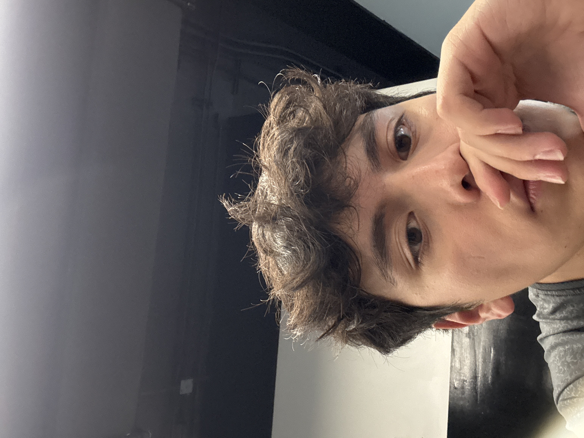 A close-up, rotated view of a person's face. The person has brown, curly hair, brown eyes, and light skin. Their hand is covering their nose and mouth. The background consists of a wall that is light to the right of the image and dark to the left of the image. The exact location in Mexico City, Mexico, cannot be determined from this image.