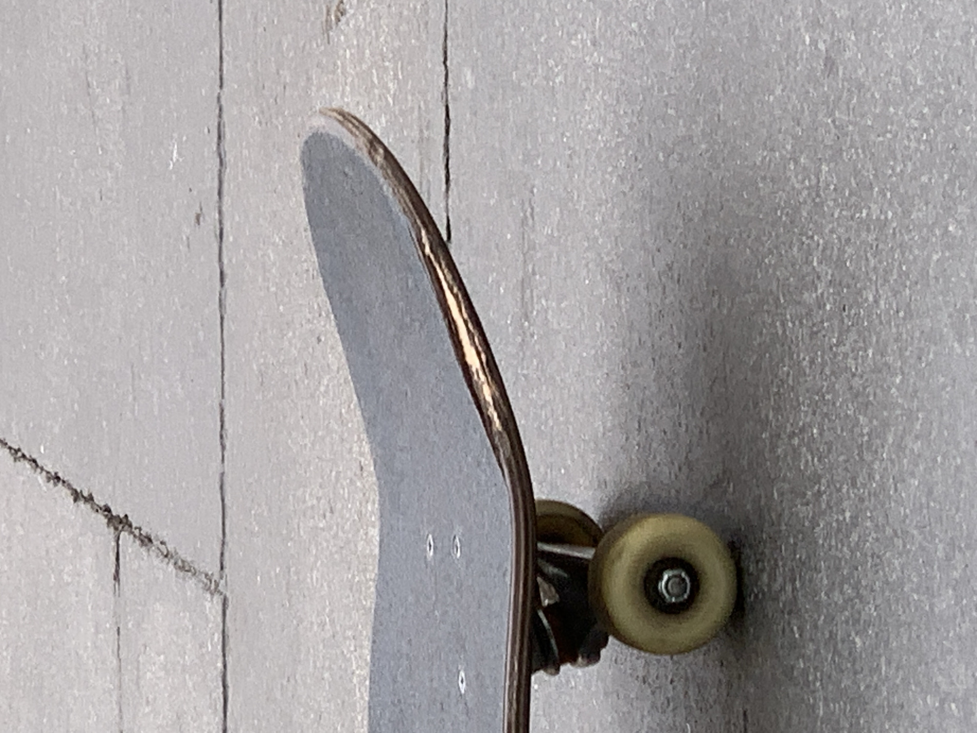 A skateboard is leaning against a textured, grey wall. The deck of the skateboard is grey and curving. A single visible wheel is yellow. The wall appears to be concrete or a similar material, with vertical lines or seams.
The image does not provide enough information to determine the location as Barcelona, Spain. There are no people, actions, or interactions visible in the image.