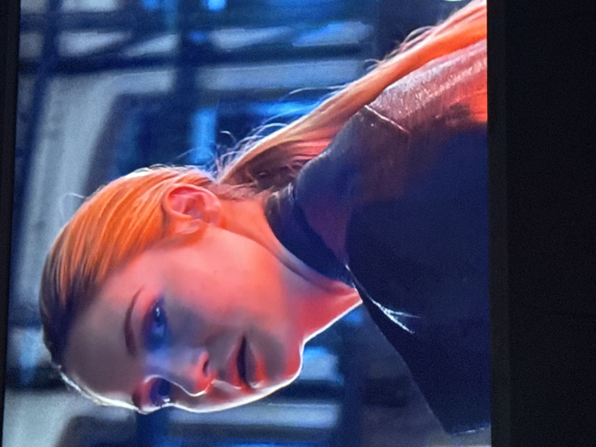 A close-up of a person's face, turned to the side, with fair skin and reddish-blonde hair. The person is wearing a dark garment. A mix of red and blue lighting illuminates the face. The background appears to be an out-of-focus interior scene with indistinct structures. There is no discernible information in the image to place it in Mytishchi, Russia or provide forensic details about actions or interactions.
