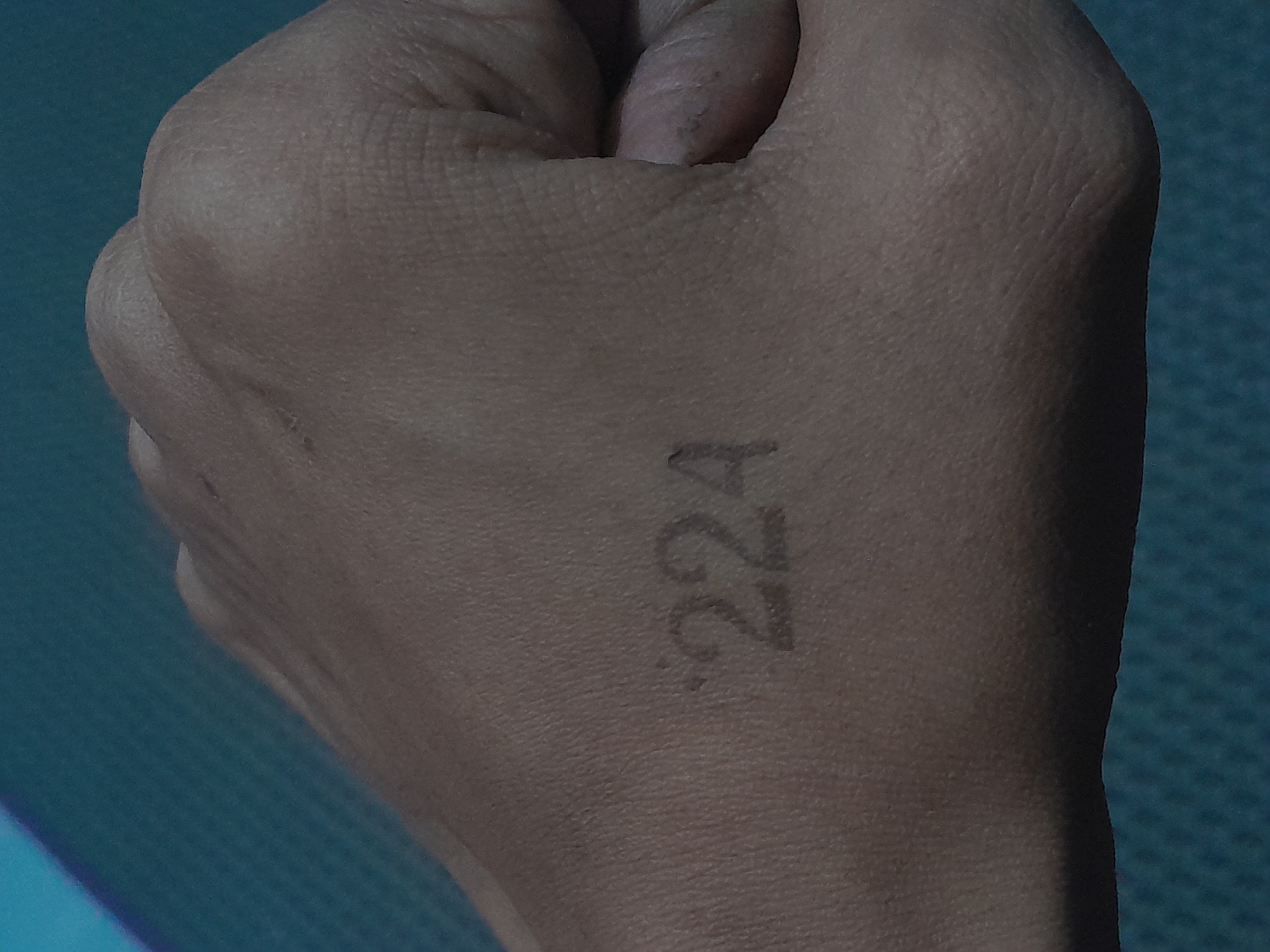 The image shows a close-up view of a person's hand with the numbers "224" marked on the back of it. The hand is resting on a textured, dark teal surface, possibly a mat or fabric. The lighting is dim, casting shadows and highlighting the texture of the skin. There is no indication of the city of Depok, Indonesia, or any other specific location in the image.
