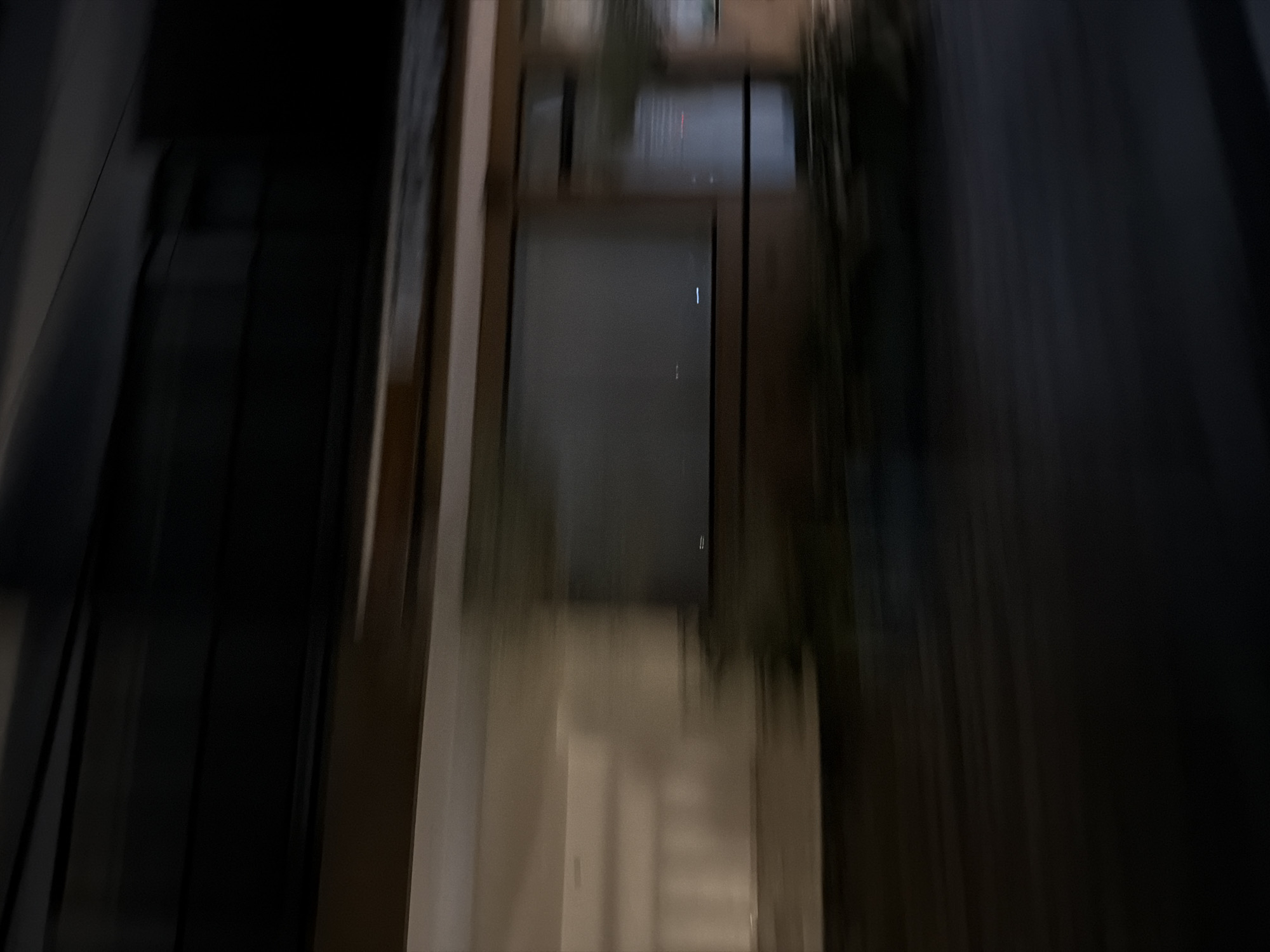 The image shows a dark and blurry view through a doorway or window. The background reveals an interior space, potentially a hallway or room. The location is indicated as North Kuta, Indonesia. The focus and clarity of the image are poor, but it shows indoor architecture with some visible details of walls and potentially more rooms extending from the main view.