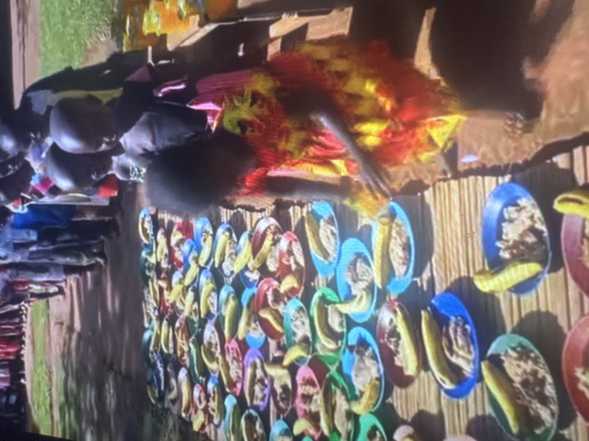 In Abuja, Nigeria, a group of children are lined up to receive food served in colorful plastic plates on the ground. The food appears to be rice or a similar grain, topped with pieces of banana. The children are dressed in various attire, and some are reaching out to receive their meals. In the background, adults are also present, suggesting a community event or a school feeding program. The setting appears to be outdoors, with a grassy area visible behind the line of children.