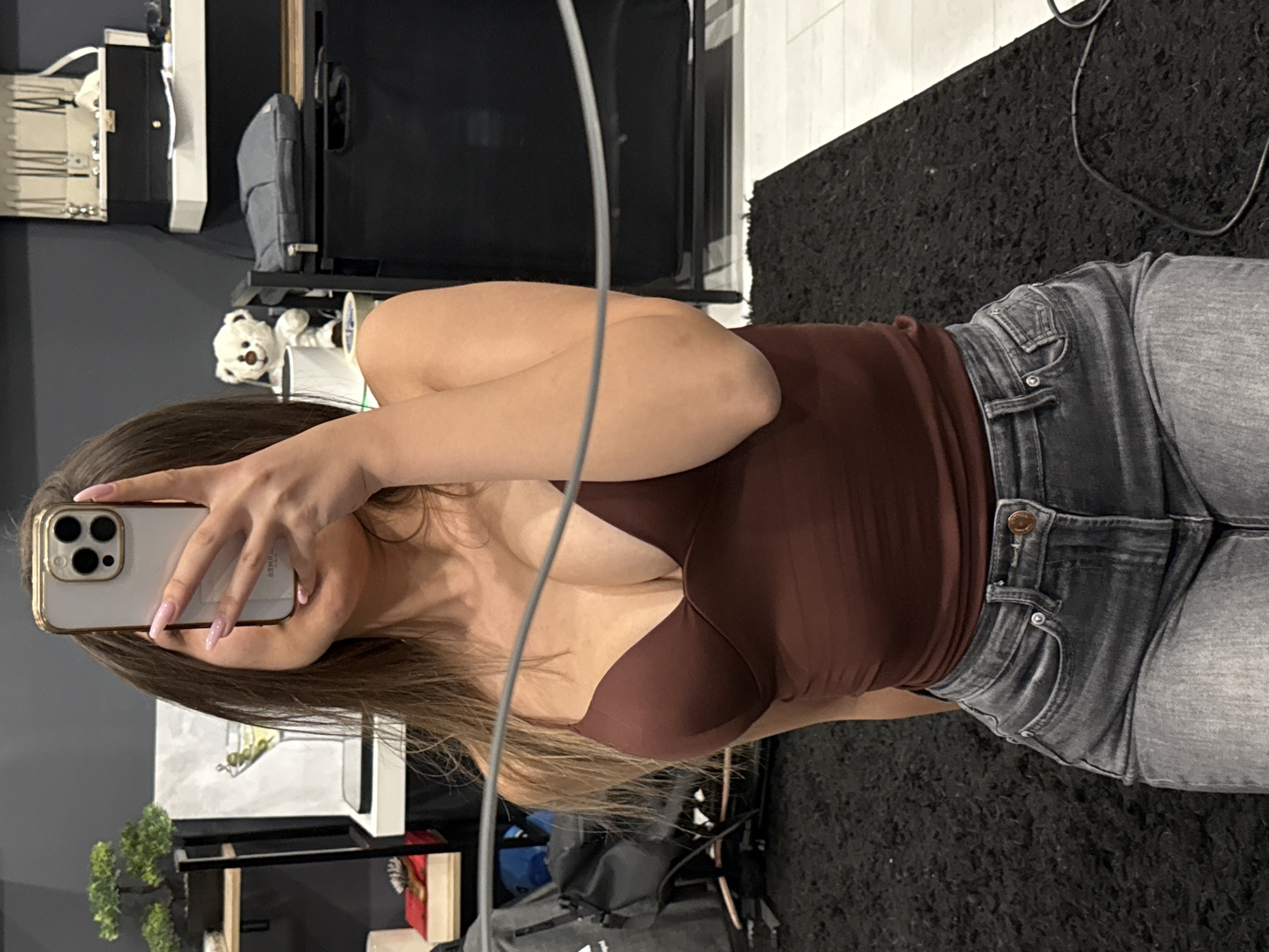 A person is visible in the image, holding a phone to take a picture. The person is wearing a brown top and gray jeans. The background includes furniture, a teddy bear, artwork, and a black rug. The location in Sofia, Bulgaria is not discernible from the image.