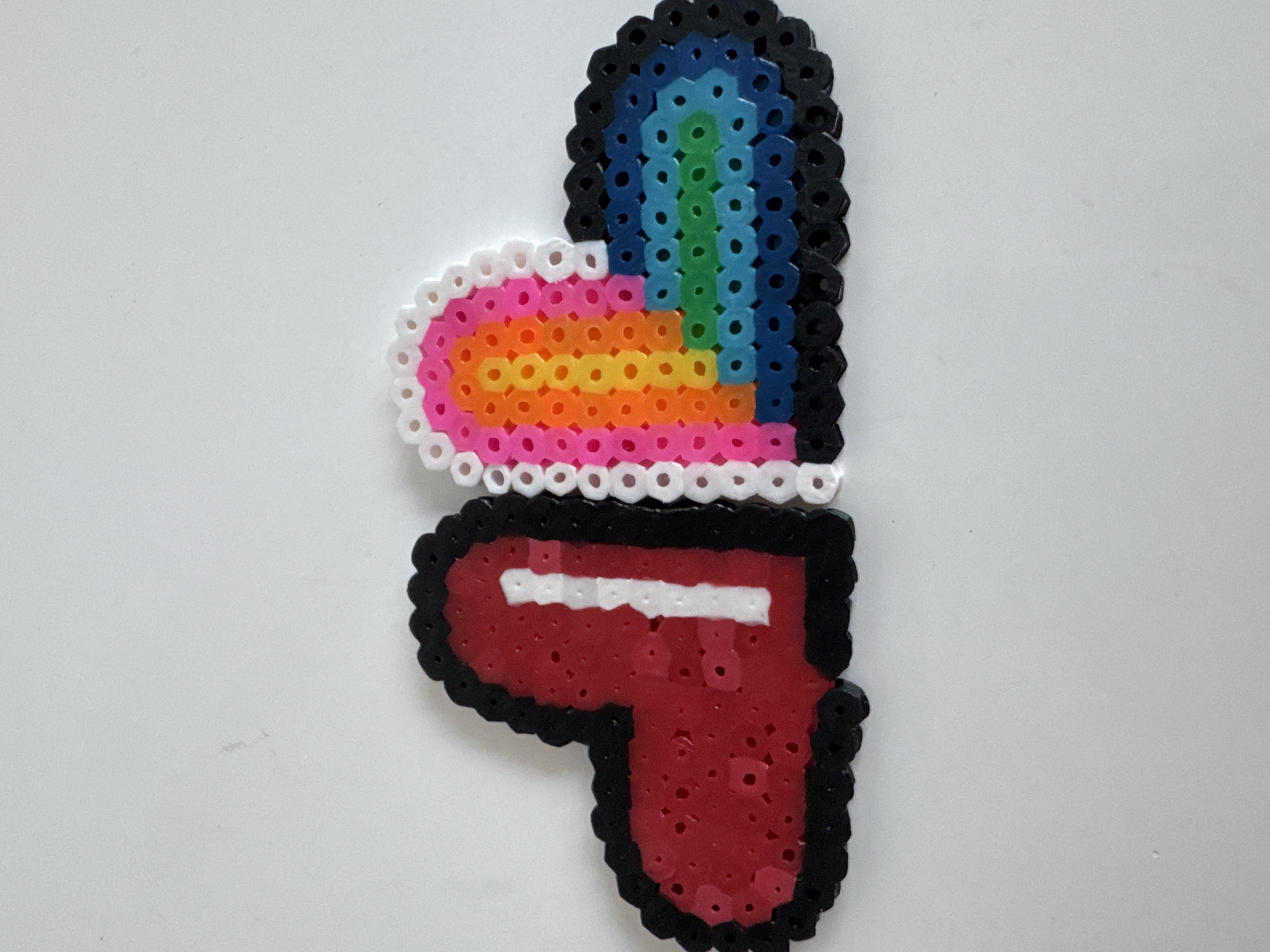The image shows two fused bead crafts. The upper craft is a heart shape, featuring a rainbow color scheme on one half and solid black on the other. The other craft is a red pistol outlined in black with a white stripe near the top. Both crafts are placed on a white surface. The image provides no information regarding the location in Bac Nha Trang Ward, Vietnam, people, actions, or interactions.