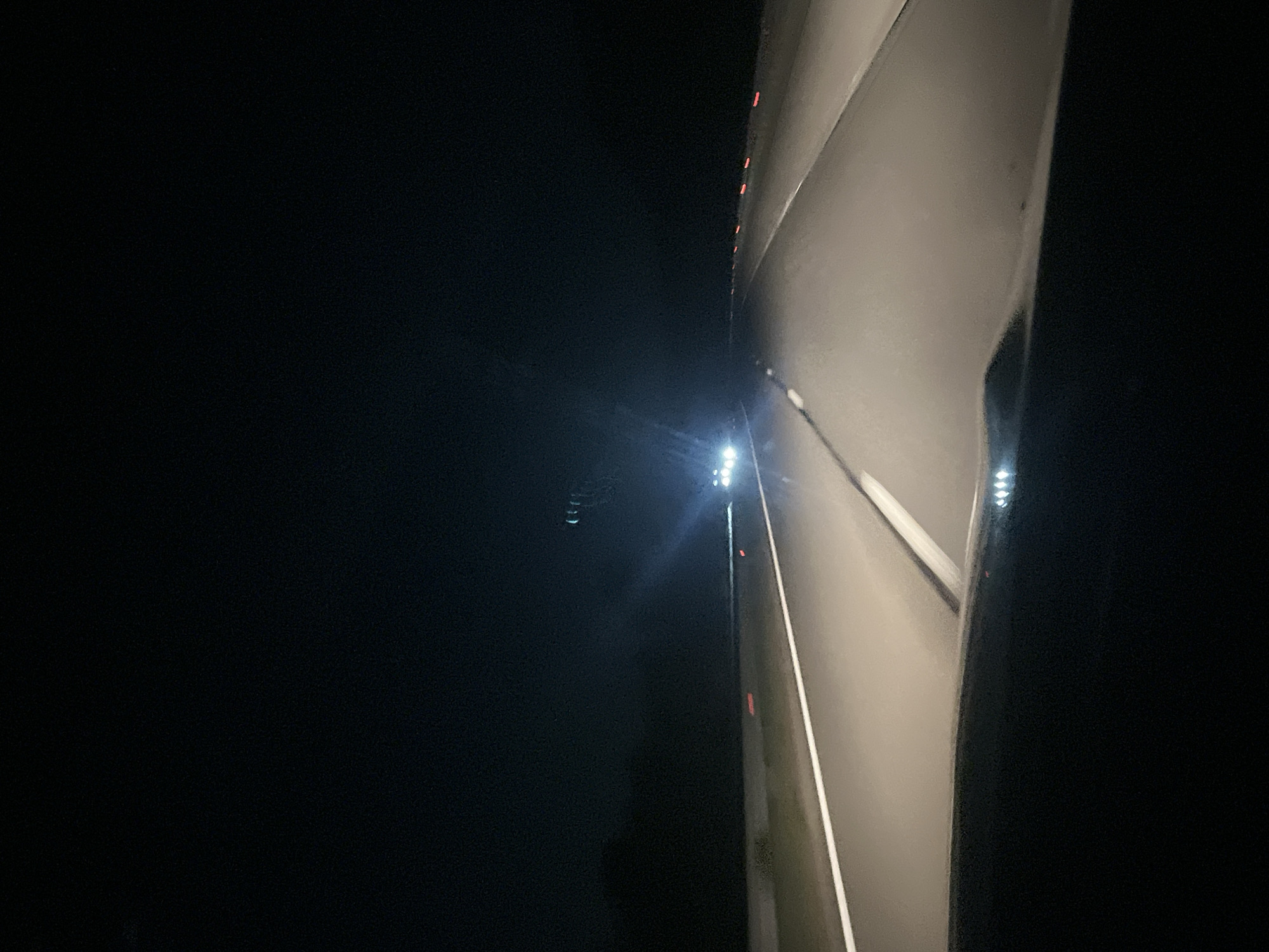 The image shows a structure illuminated by white lights at night. The structure appears to be concrete or a similar material, with linear elements suggesting a road or path. To the left of the structure is darkness and the sky is visible. Red lights can be seen on the edge of the structure. The scene seems to be in Blajievo, Bulgaria based on the instructions, though there is no visual information in the photo that indicates the location.