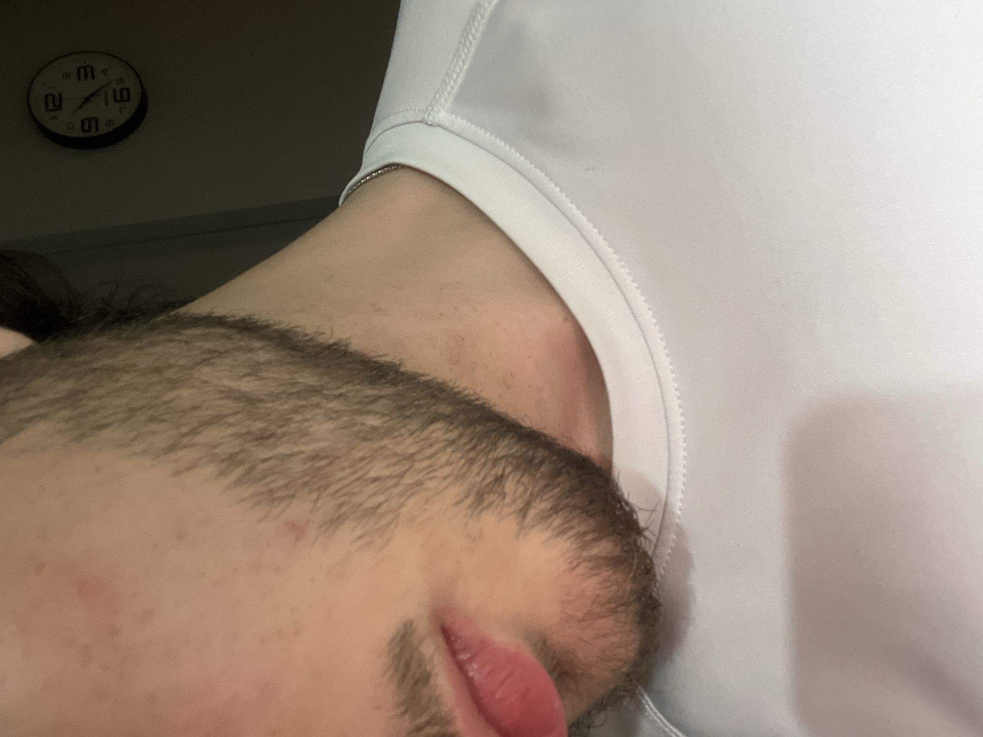 The image shows a close-up of a person's face, specifically the forehead, hairline, and part of the beard and lips. The person is wearing a white shirt. A wall clock is visible in the background, partially obscured. It is difficult to determine the location in the city of Yerevan, Armenia based solely on this image.