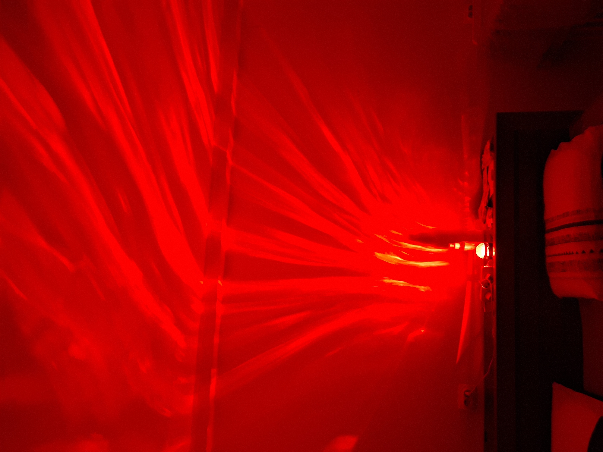 An interior view illuminated predominantly by red light. Light rays emanate from a source near a doorway. A partially visible object is positioned near the doorway. The location in the city of Novi Sad, Serbia, is not discernible from the image.