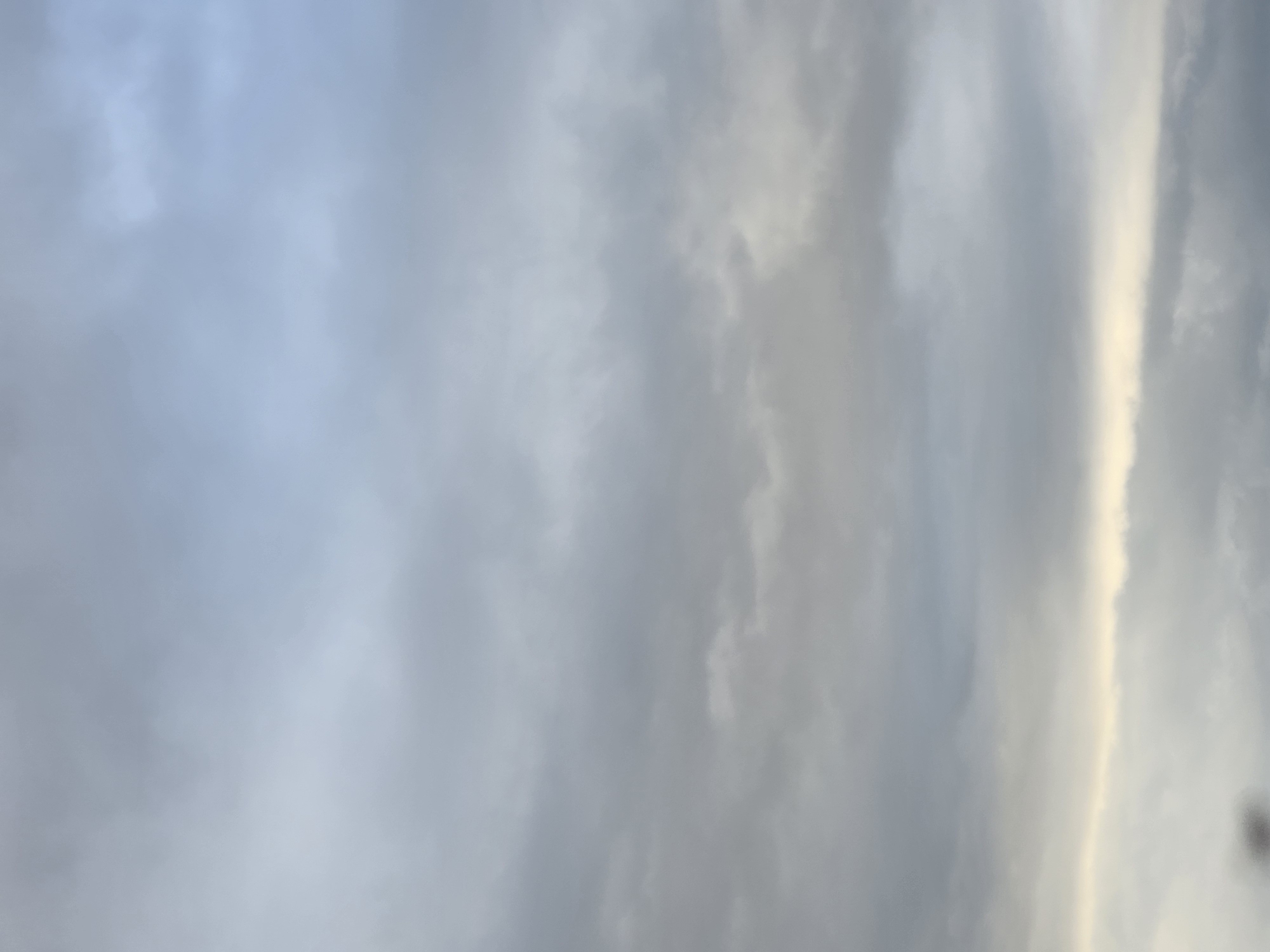 The image depicts a sky filled with predominantly gray and white clouds. A vertical band of light, possibly sunlight, cuts through the clouds on the right side of the frame. The overall impression is that of an overcast or stormy sky. The location is unknown.