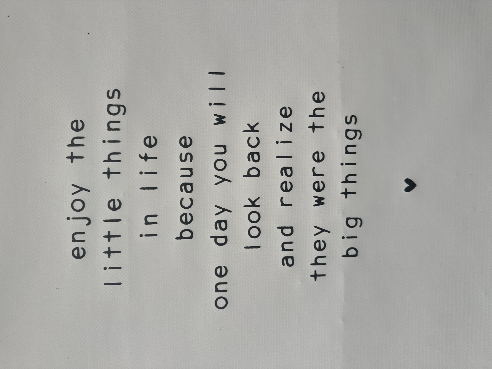 The image shows a white textured surface with black text printed on it, arranged in lines. The text reads: "enjoy the little things in life because one day you will look back and realize they were the big things." A small black heart is printed below the text. The background is a uniform white with a subtle texture. There are no people, animals, or any other objects present. The context of Giethoorn, Netherlands, is not discernible from the image.