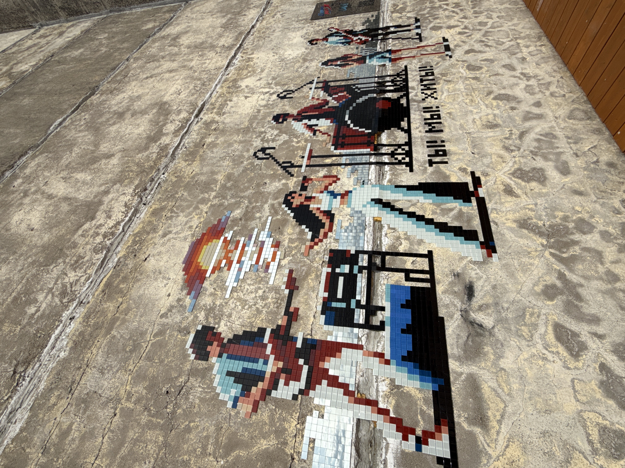 The image shows a mosaic on a concrete surface. The mosaic is of several figures from the 1991 movie "Only Old Men Are Going to Battle" (В бой идут одни «старики») by Leonid Bykov. The mosaic is on the side of a building in Saint Petersburg, Russia. The mosaic shows the main characters flying with the text: "You! We! We live!" from the song performed in the movie.