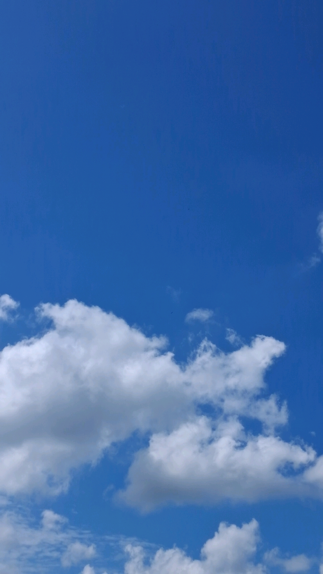 The image shows a clear blue sky with scattered white clouds. The clouds are cumulus and are situated in the lower portion of the frame. The sky appears bright and sunny. There are no visible landmarks or objects that would indicate a specific location within the city of Hanamkonda, India. The scene is entirely composed of sky and clouds.