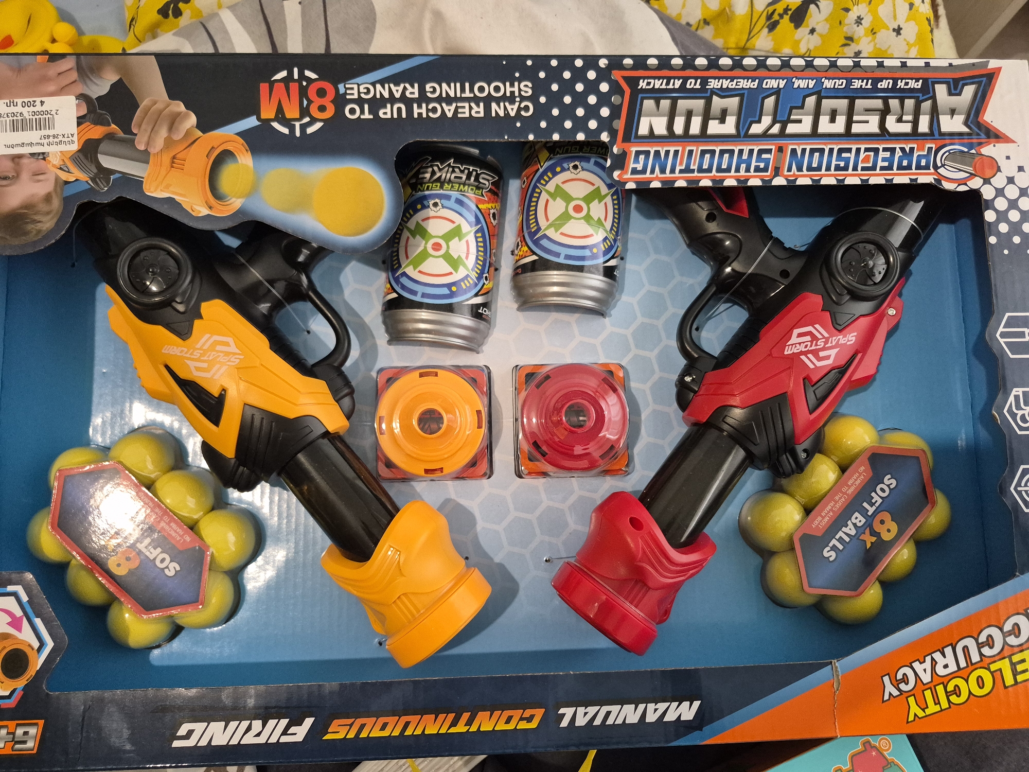 This media file displays an "AIRSOFT GUN PRECISION SHOOTING" toy set, presented in its retail packaging. The set features two distinct toy guns: one in orange and black, and the other in red and black, both labeled "SPLAT STORM". These guns are described as "MANUAL CONTINUOUS FIRING" with "ELOCITY ACCURACY".
The package includes numerous accessories for play. There are two sets of "8x SOFT BALLS" each, in a bright yellow color. A safety notice on the packaging assures that "LAUNCHING CAUSES ALMOST NO HARM TO THE HUMAN BODY". For target practice, the set provides two cylindrical "POWER GUN STRIKE" cans with bullseye designs, along with two smaller, flat round targets, one orange and one red.
Prominent text on the packaging highlights key features: the guns "CAN REACH UP TO 8M SHOOTING RANGE" and the recommended age is "6+". A graphic depicts a child's hand aiming one of the toy guns, and an instruction reads, "PICK UP THE GUN, AIM, AND PREPARE TO ATTACK".
A partially visible price tag in the upper left corner indicates the product is a "զենքերի հավաքածու" (weapon set/collection) with product code "ATX-26-657" and a price of "4 200 пр.", likely referring to 4200 Armenian Dram, consistent with the Yerevan, Armenia context.