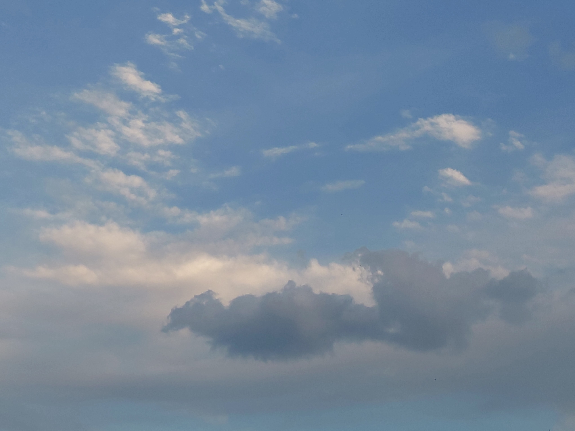 This is a daytime photograph of a cloudy sky. The sky is a pale blue with scattered white and grey clouds. The clouds vary in density, with some appearing wispy and translucent, while others are thicker and more opaque. The lower portion of the image shows a thicker layer of clouds, tinged with a soft, warm light, suggesting it might be near sunrise or sunset. No specific landmarks or urban features are visible, making it impossible to identify a precise location within Samara, Russia. The image captures a natural atmospheric scene.