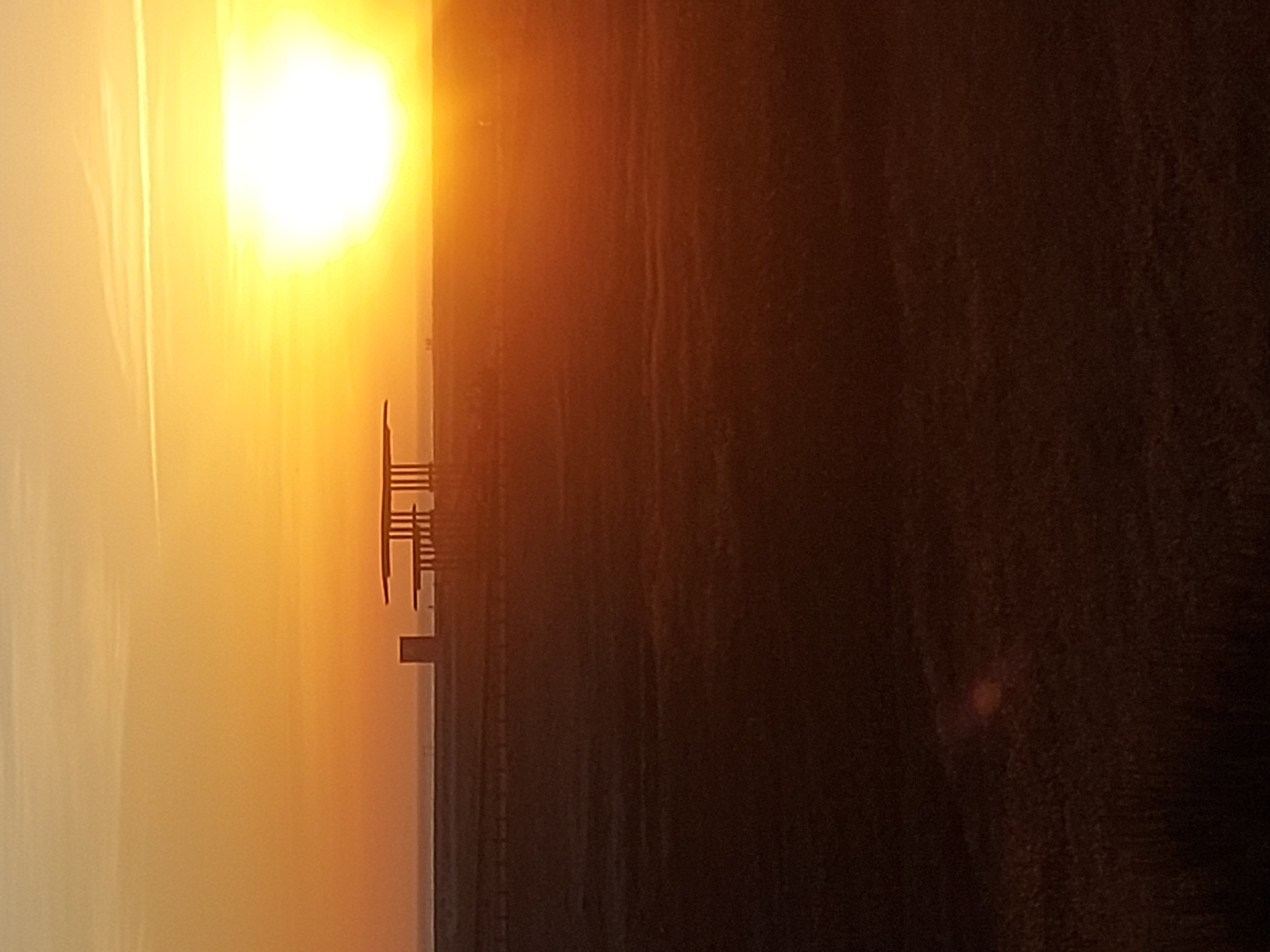 The image shows a landscape at Figueira da Foz, Portugal, during sunset. A pier stretches into the water, its structure silhouetted against the bright sun. The sky is filled with the warm hues of orange and yellow. The ground is a dark mass, likely sand.