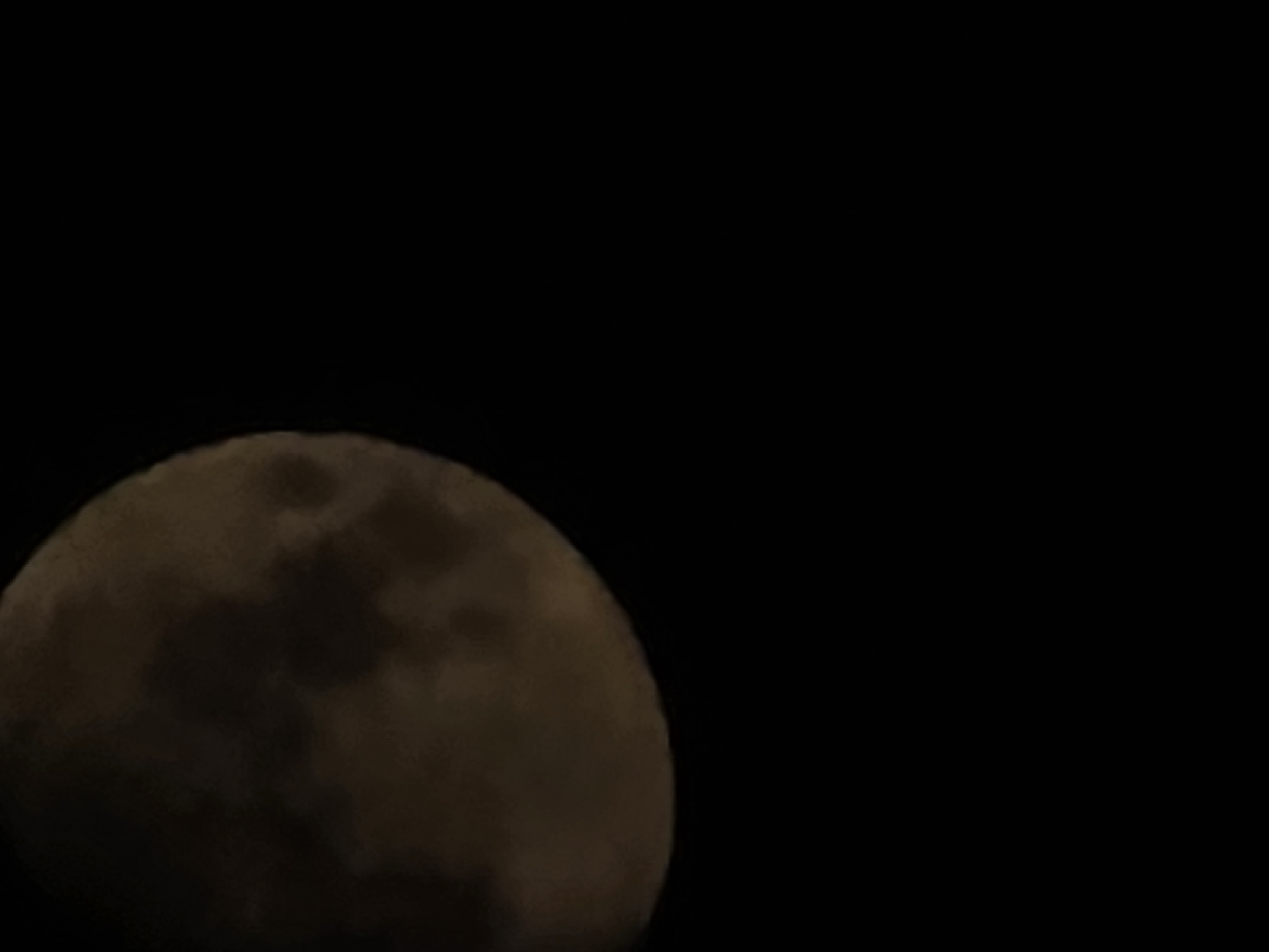 The image is a close-up, slightly out-of-focus shot of a full moon against a black sky. The moon is partially illuminated, revealing dark patches that are likely lunar maria. The bottom two-thirds of the image are entirely black, with no visible context of the surrounding environment. There is no indication of the city of Yambol, Bulgaria, or any other geographical location within the image. The image contains no people, subjects, objects, or actions other than the moon itself.
