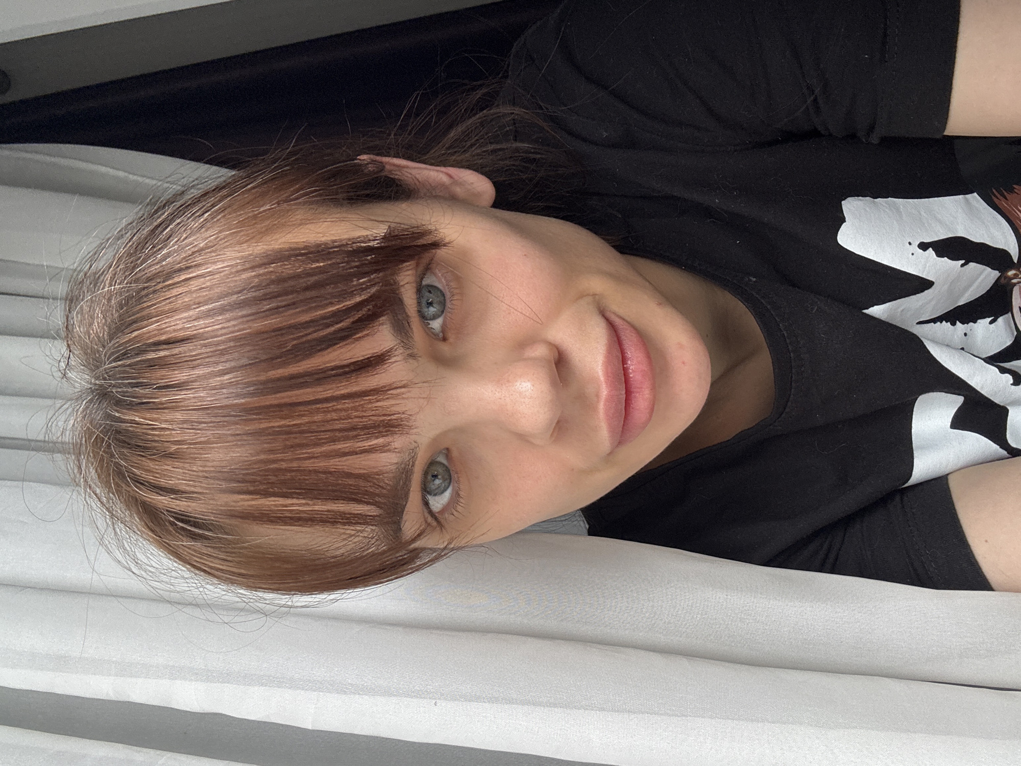 A woman with light complexion and hazel eyes, wearing a black t-shirt, is lying on a white surface, possibly a bed or a similar soft furnishing. The location, Rostov-on-Don, Russia, is not discernible from the image content.