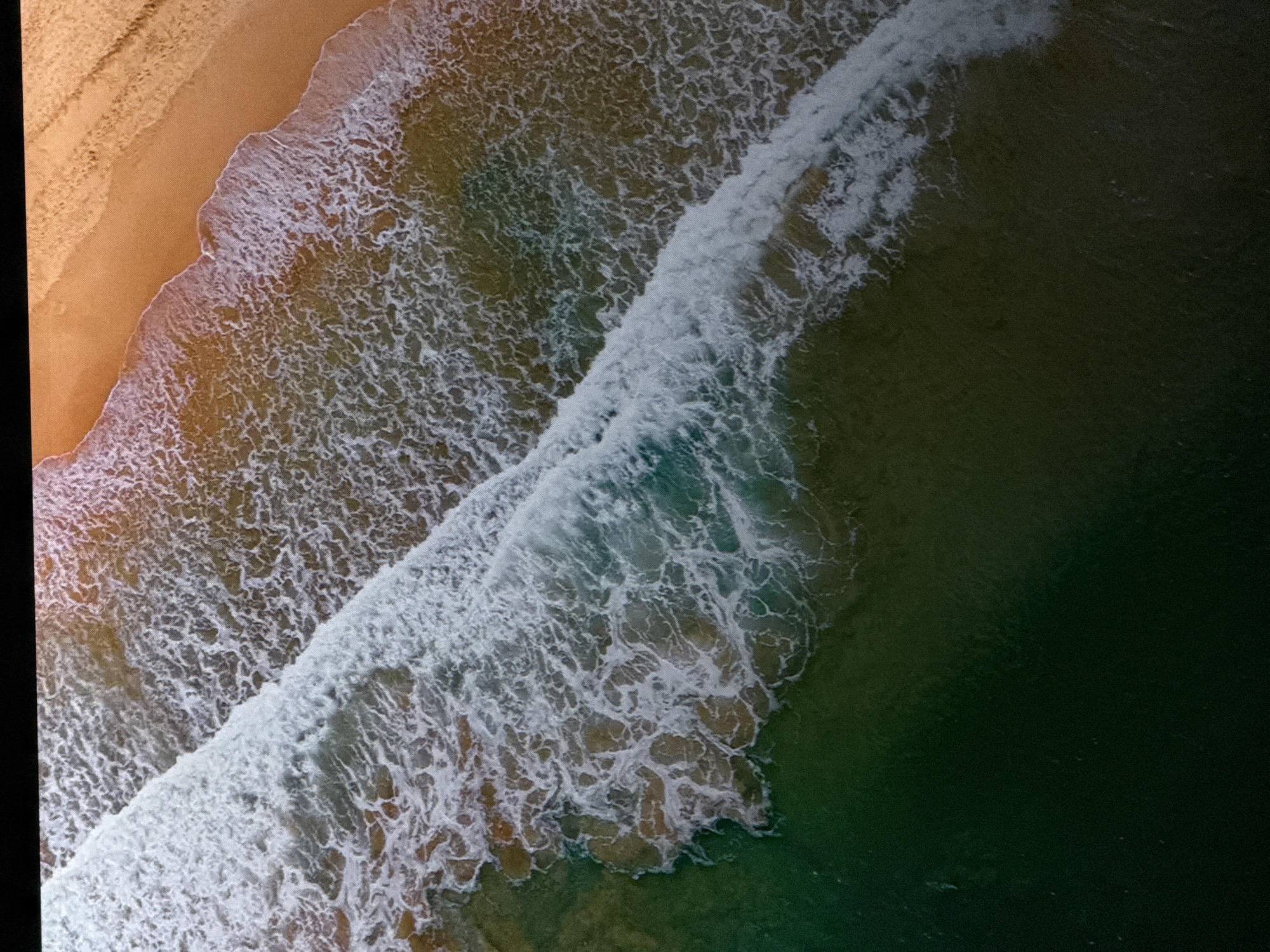 The image is an aerial view of a beach with waves crashing on the shore. The sand is golden and the water is a mix of green and blue. The waves are white and foamy, and they are breaking in a diagonal line across the image. The image is well-lit and the colors are vibrant. The location in Saratov, Russia is not identifiable from the image.