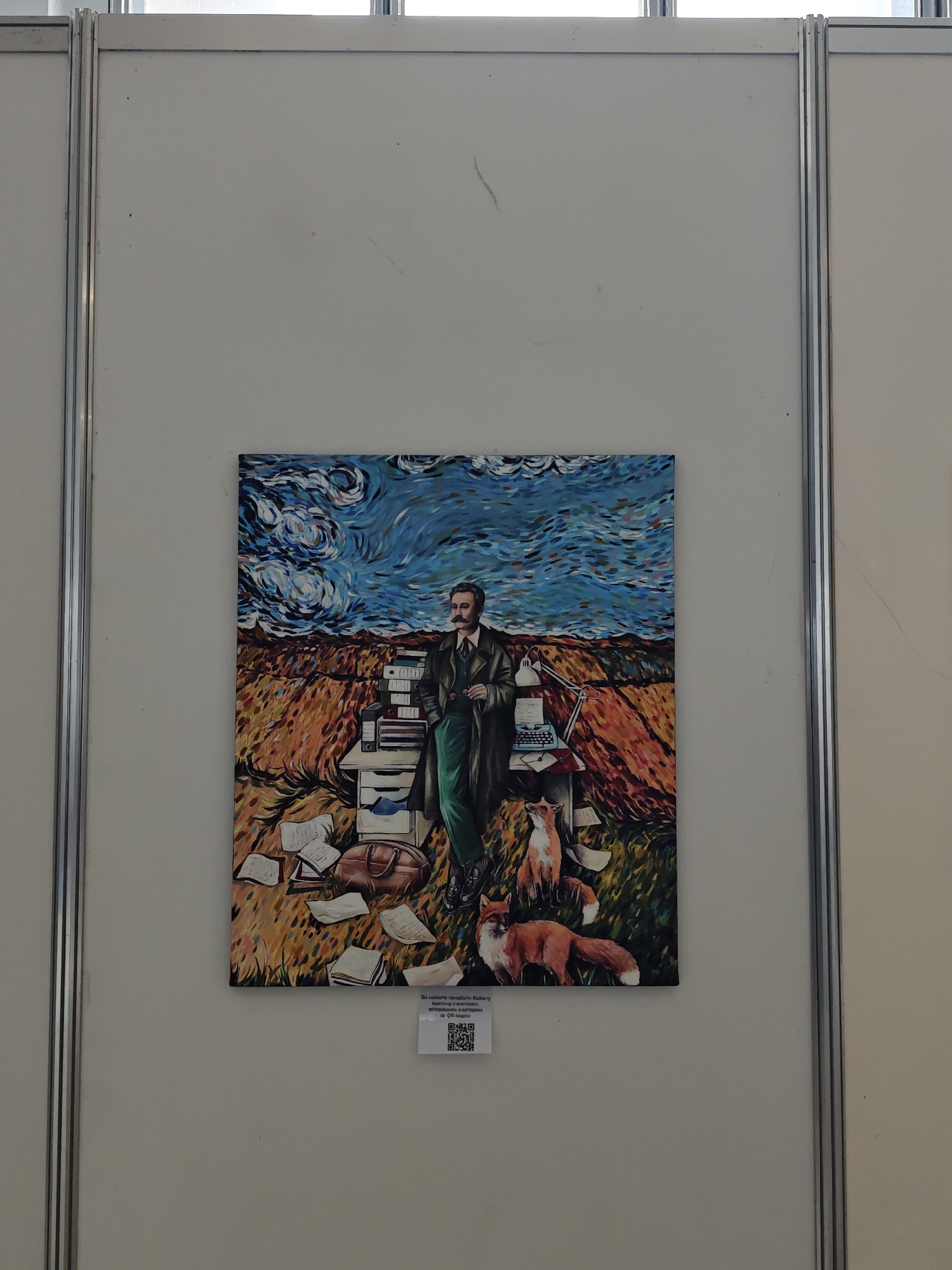 The image shows an impressionistic painting of a man with a mustache in a green suit standing amidst a wheat field, flanked by a stack of books and a vintage typewriter. Two foxes are depicted at his feet. The sky above is rendered in swirling blues and whites, reminiscent of Van Gogh's style.
The painting is displayed on a white wall, framed by metal poles, suggestive of an art exhibition or gallery setting. A small sign with text and a QR code is affixed below the painting. While the image doesn't provide explicit clues about the exact location, the mention of Kyiv, Ukraine, suggests it might be an art gallery or exhibition space within that city.