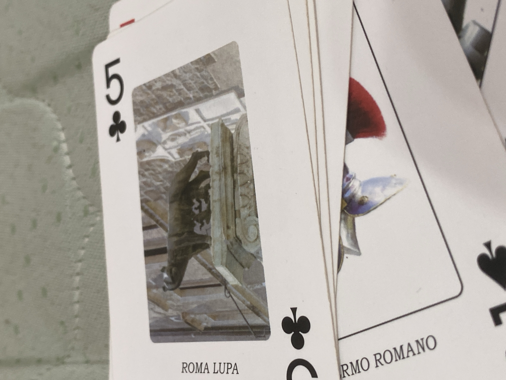 The image shows a stack of playing cards. The top card is the 5 of Clubs. The image on the card appears to be a photograph of the Capitoline Wolf, a bronze sculpture depicting a she-wolf suckling Romulus and Remus, mythical founders of Rome. The text "ROMA LUPA" is printed below the image. The location in the city of Poltava, Ukraine is not included in this image.
