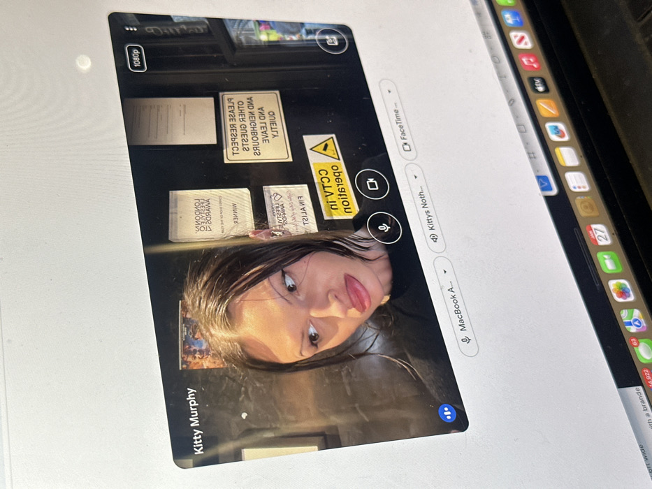 A screen displays a FaceTime call with Kitty Murphy. The person on the screen is sticking their tongue out. Behind them are several signs, including one warning about CCTV operation and another advising people to respect neighbors and leave quietly. A Macbook interface surrounds the call screen. The Macbook has several icons, including the calendar. A 1080p indicator is in the top left corner of the screen.